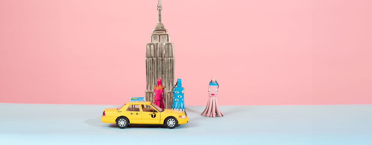 A display featuring "Squid Charms" by Min & Mon, a NYC-based brand, includes a yellow toy taxi and a mini Empire State Building. The colorful charms, shown in pink, blue, and red, highlight the brand's unique accessories.