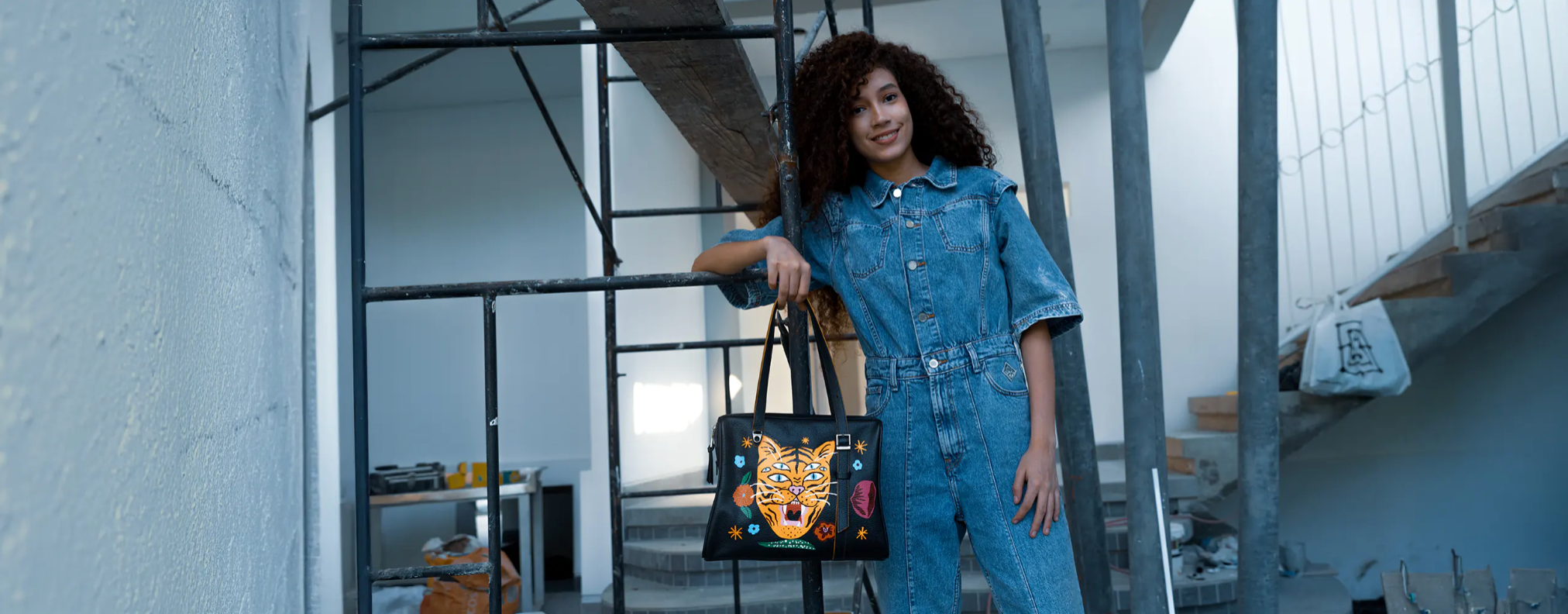 Promotional image for Min & Mon, a NYC-based brand, featuring a "Buy One Get One 50% Off" offer. Highlighted products include a black handbag with eye designs, a tiger print bag, a pink tassel charm, and various accessories.