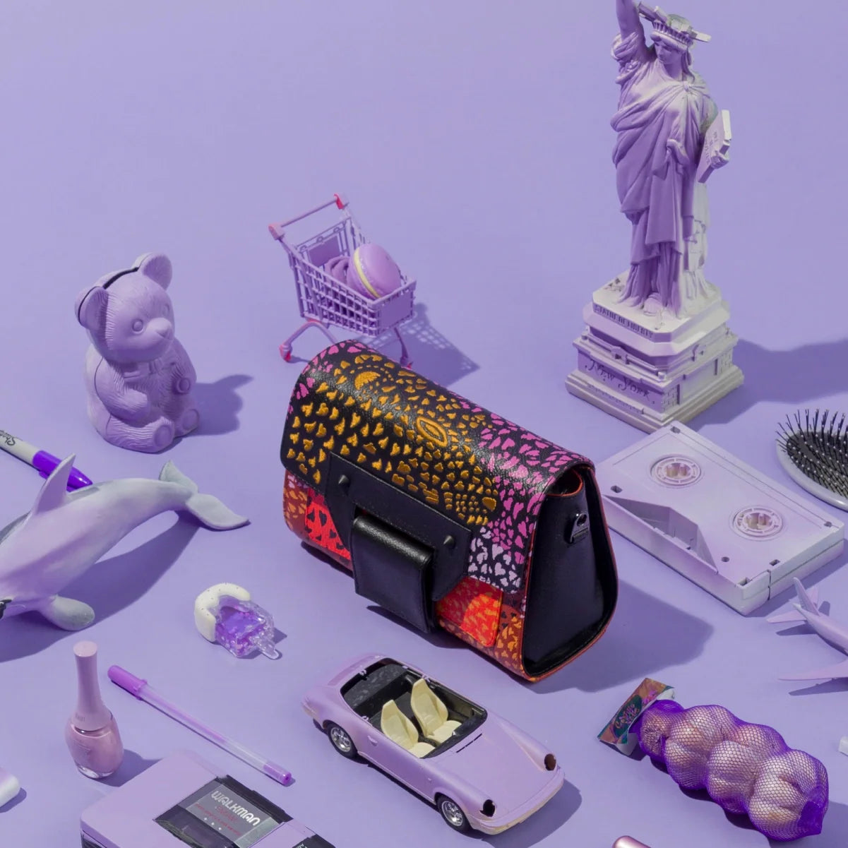 Close-up of the Min & Mon Cael bag with a vibrant multicolor print and black leather details, styled with purple toys and miniature New York City landmarks.