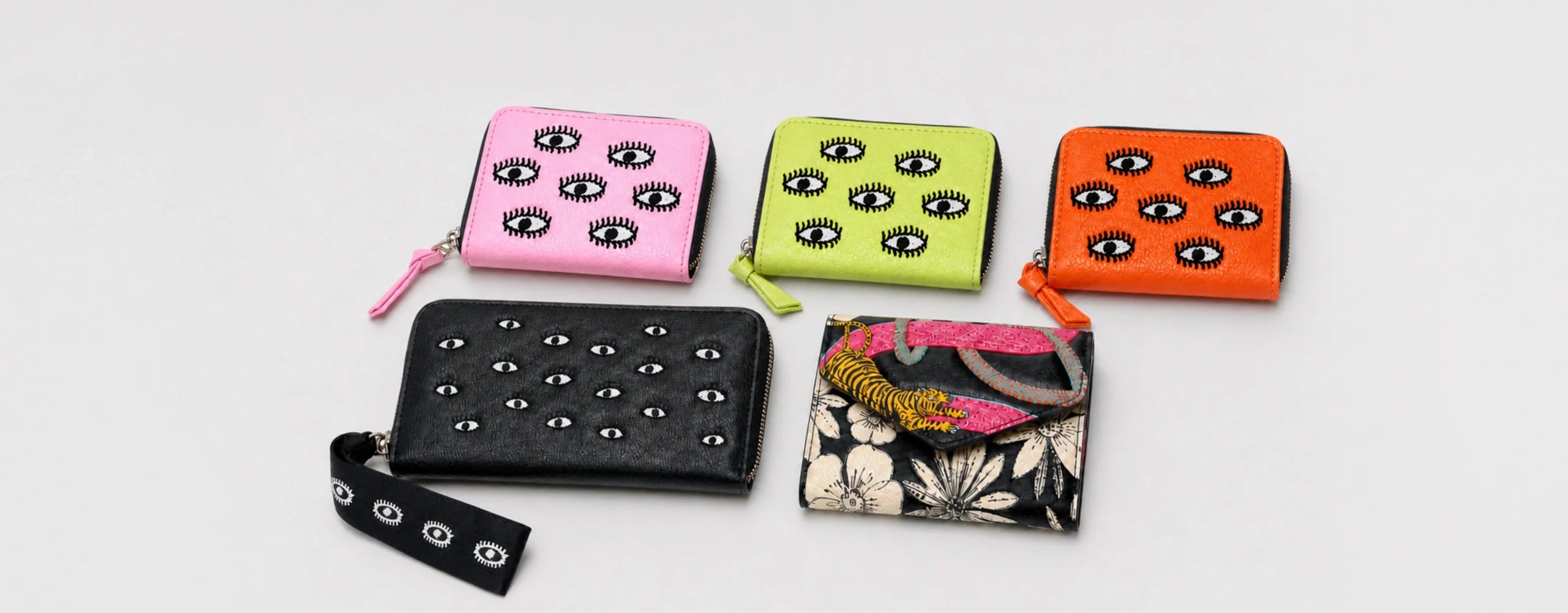 Close-up of a Min & Mon zip wallet with tiger embroidery held in front of a colorful floral mural.