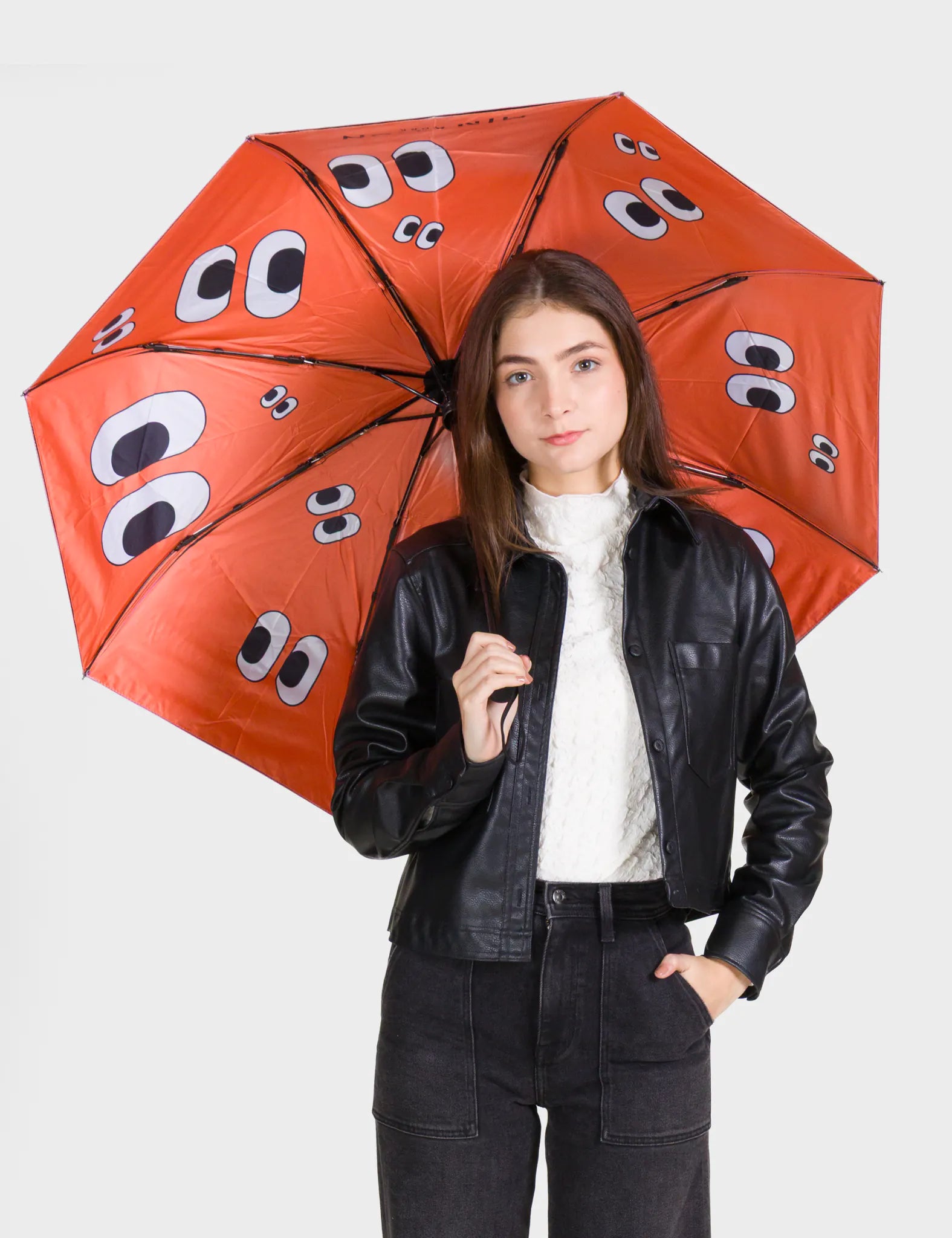 Person holding a red umbrella with googly eye design on a white background