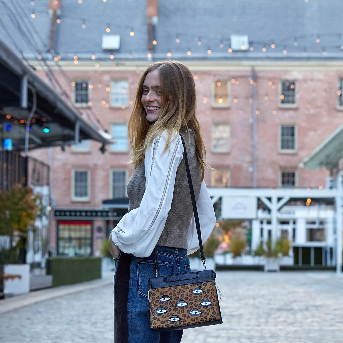 Smiling model wearing a Min & Mon animal print crossbody bag with embroidered eye details, styled outdoors in an urban setting.