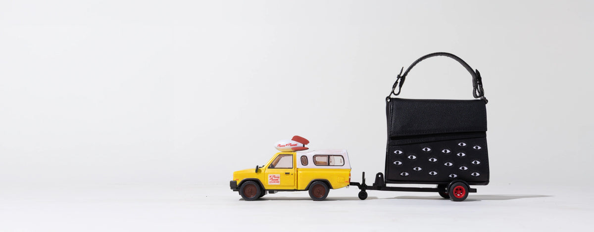 Min & Mon black Anastasio leather handbag with signature eye details on a playful miniature trailer.