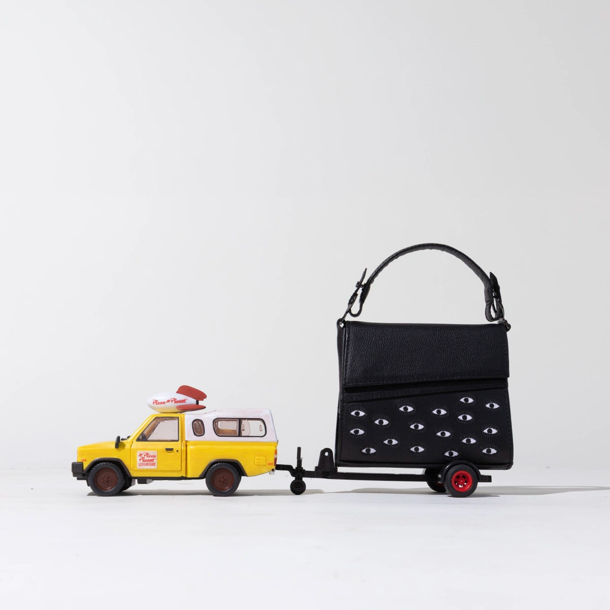 Min & Mon black Anastasio leather handbag with signature eye details on a playful miniature trailer.