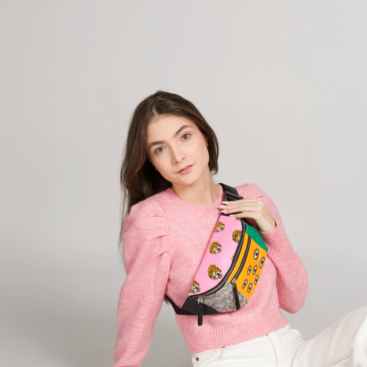 Close-up of a model wearing a playful Min & Mon crossbody bag with tiger and eye prints, styled with a pink sweater.