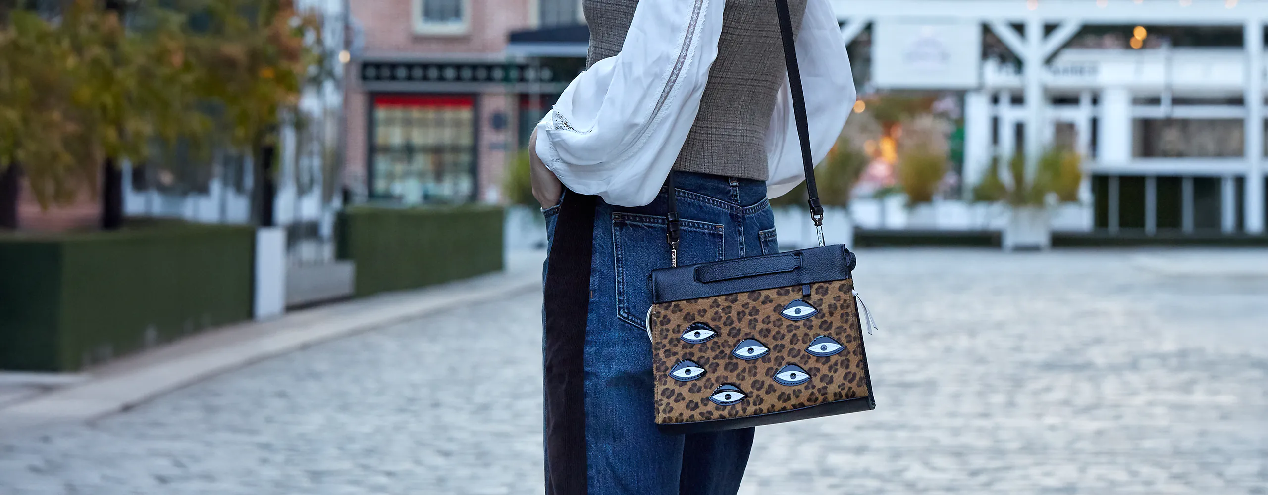 Model wearing a Min & Mon crossbody bag with animal print and embroidered eye details, styled in an urban street setting.