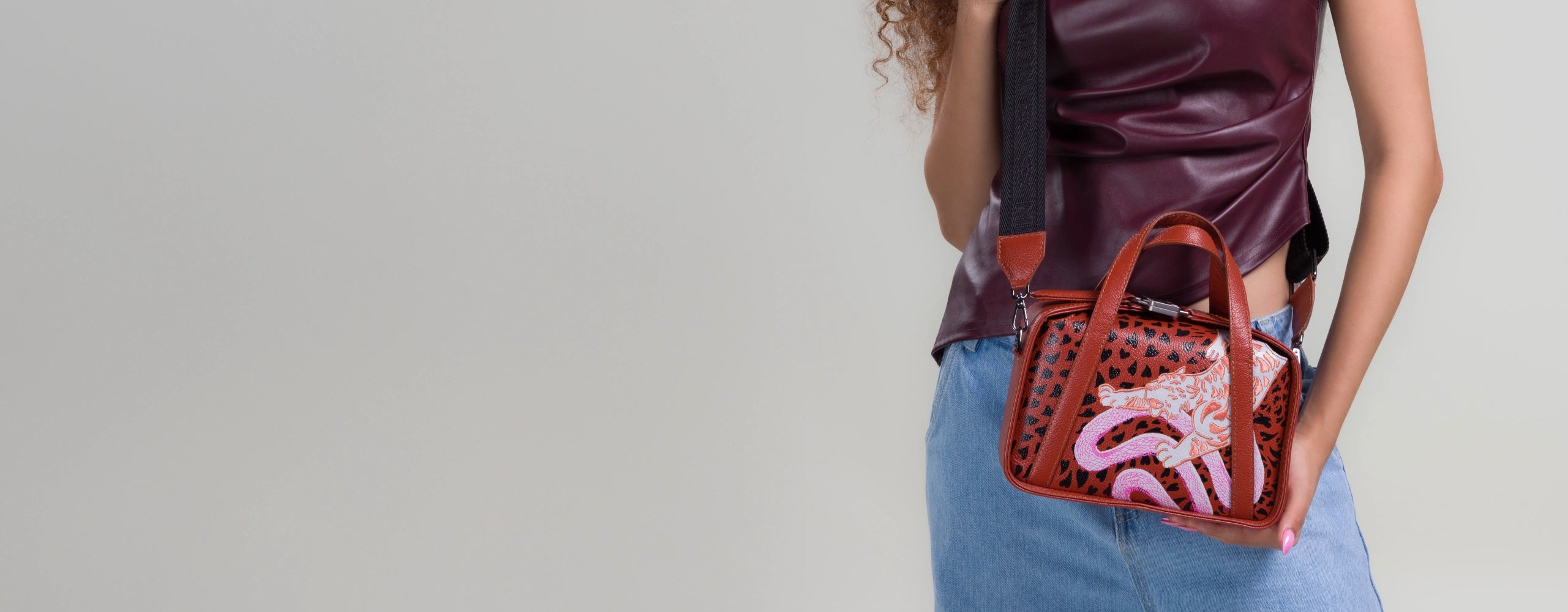 Woman wearing a burgundy top carrying a brown leather crossbody handbag with playful artwork by Min & Mon.