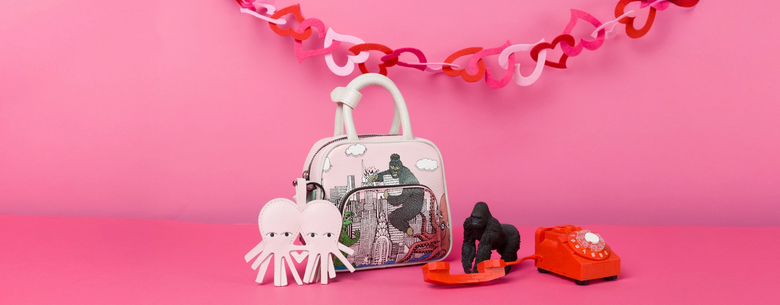 Min & Mon illustrated handbag styled with playful props and leather charm on a pink background, part of the Sale collection.