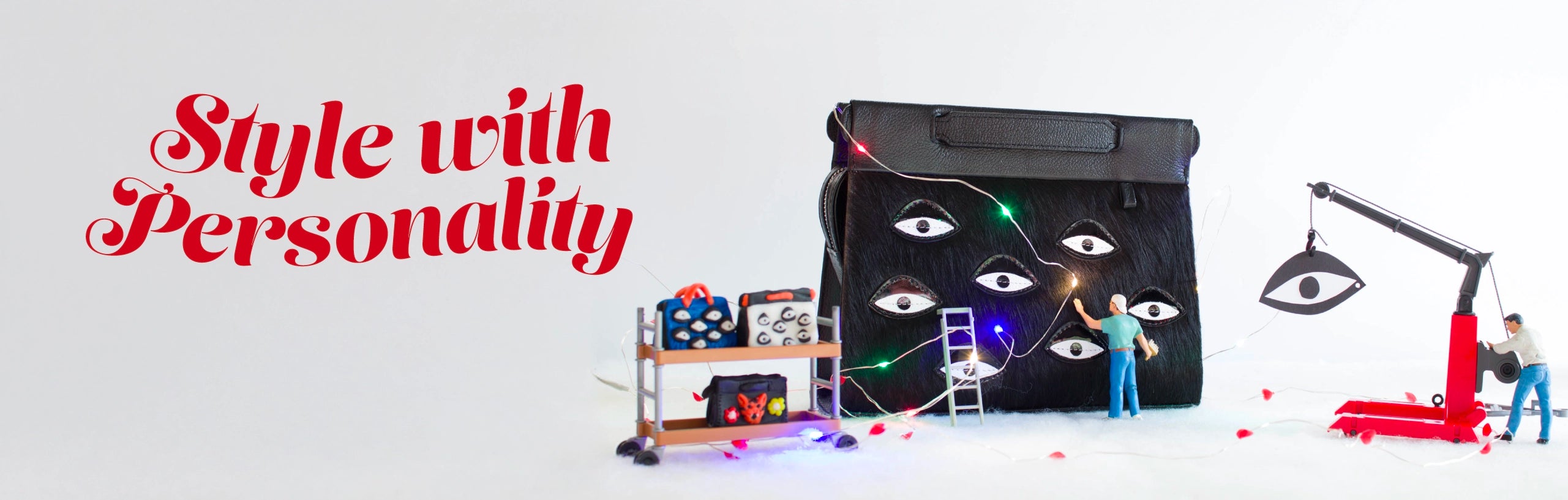 Black Min & Mon handbag with eye motifs, surrounded by miniature workers and tiny shelves with bags, lit by festive string lights.