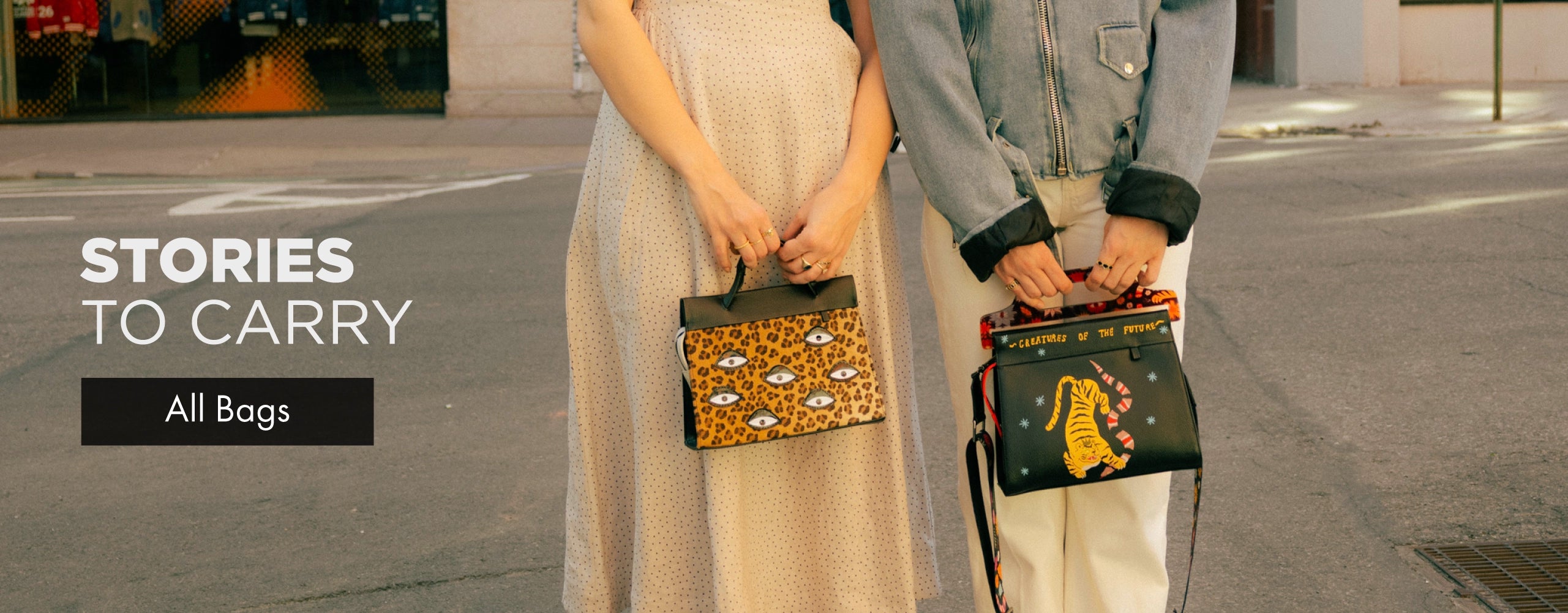 Two women standing on a New York City street holding patterned Min & Mon handbags with the text “Stories To Carry.”