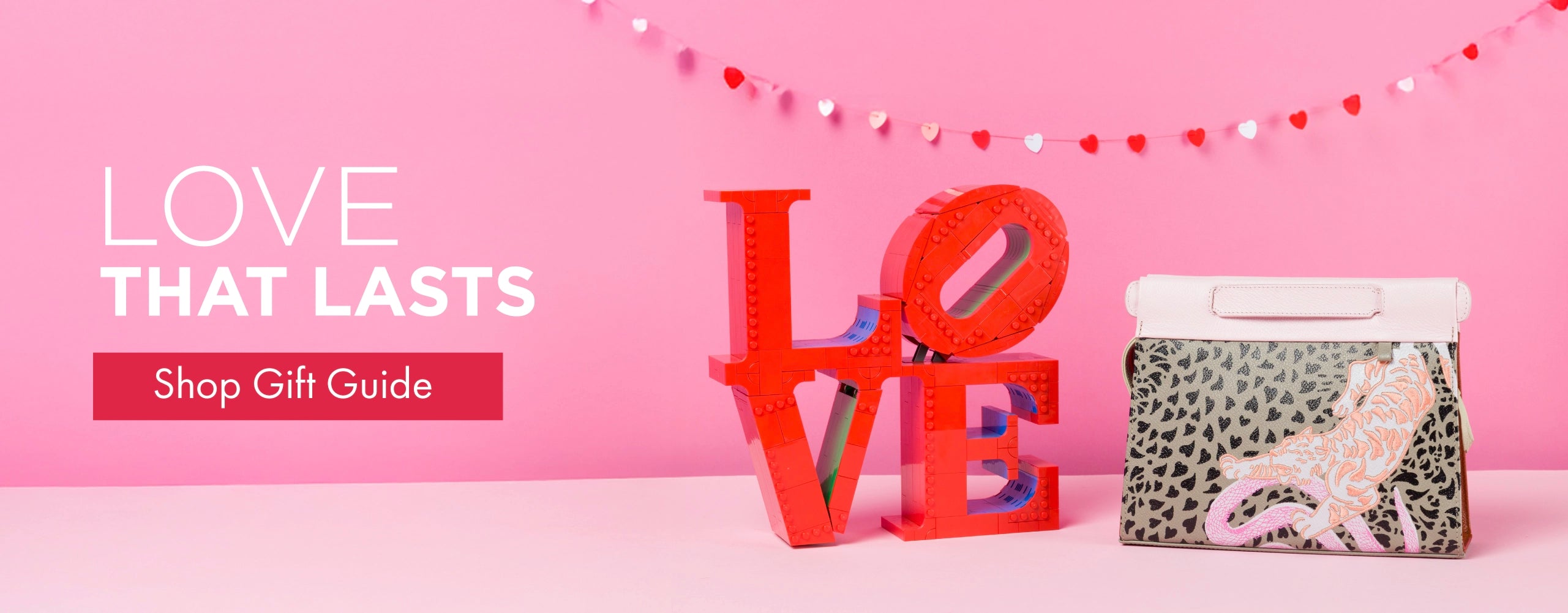 Valentine’s gift guide banner featuring a Min & Mon handbag next to a LOVE sculpture on a pink background