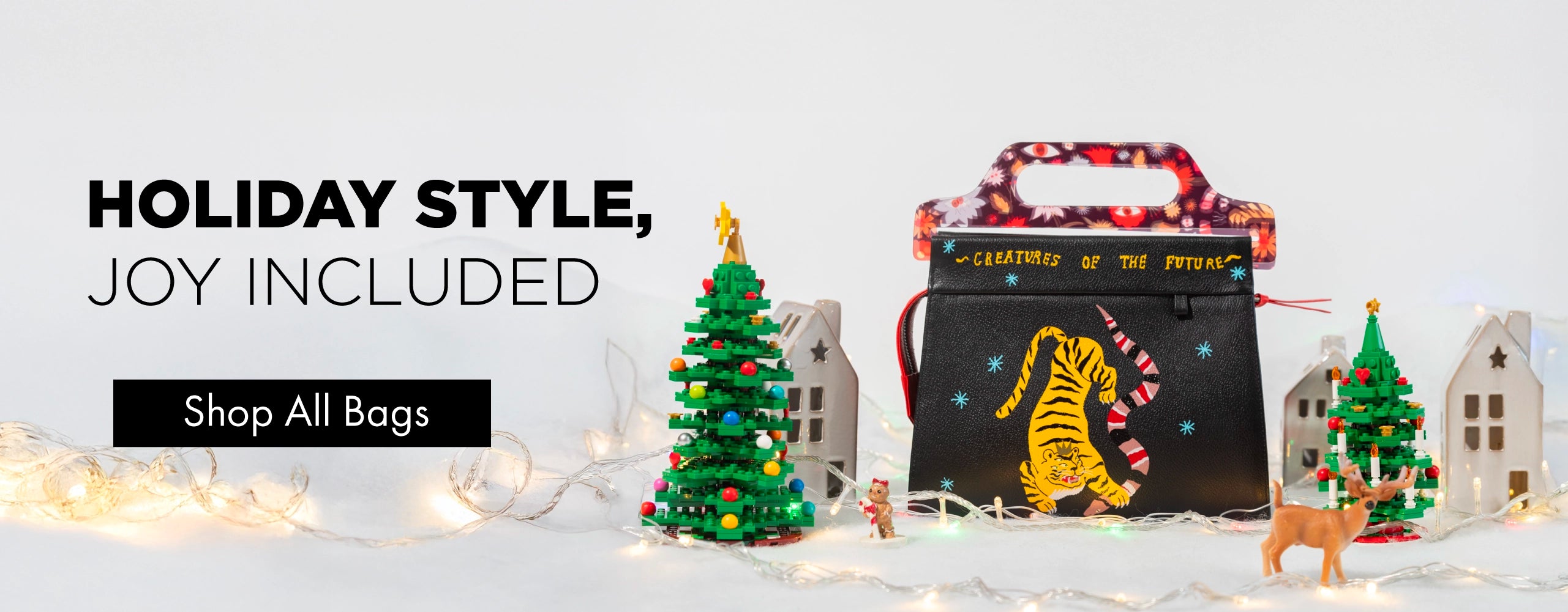 Holiday scene featuring a black Min & Mon handbag with embroidered tiger, surrounded by Christmas trees, lights, and festive decorations.