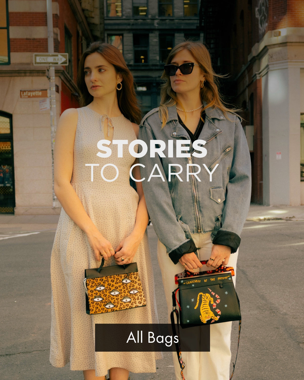 Two women standing on a New York City street holding patterned Min & Mon handbags with the text “Stories To Carry.”