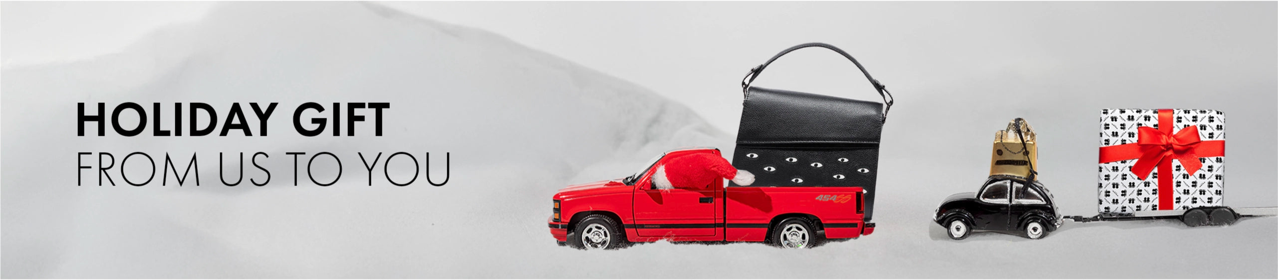 Holiday Gift From Us to You banner featuring Min & Mon bags carried by toy cars and a wrapped gift on a light background.