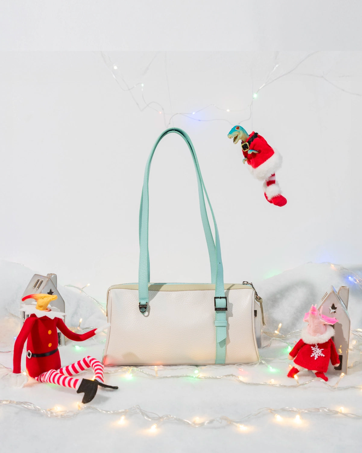 Cream leather bag with light blue straps surrounded by Christmas lights and whimsical holiday characters in a winter-inspired setting.