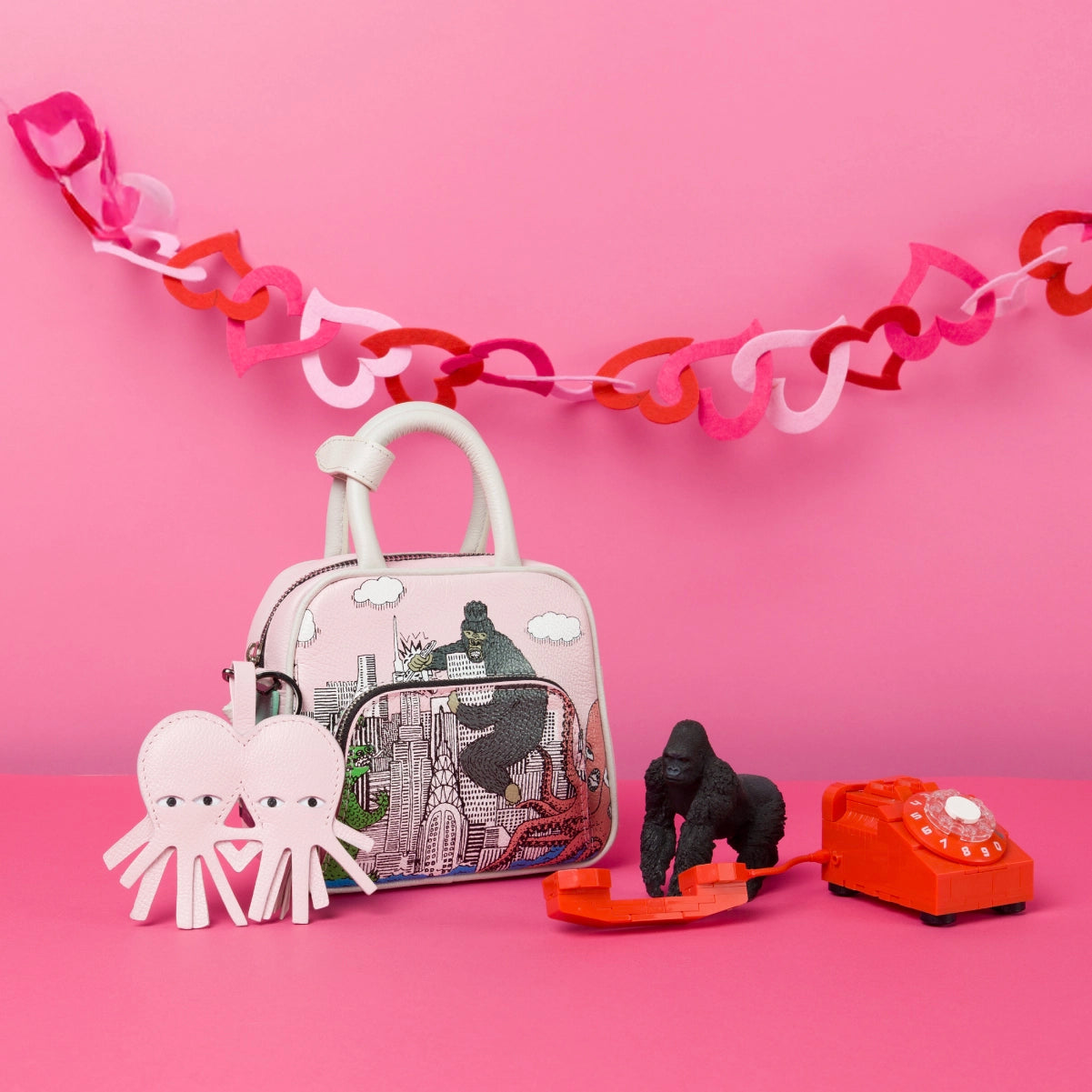 Min & Mon illustrated handbag styled with playful props and leather charm on a pink background, part of the Sale collection.