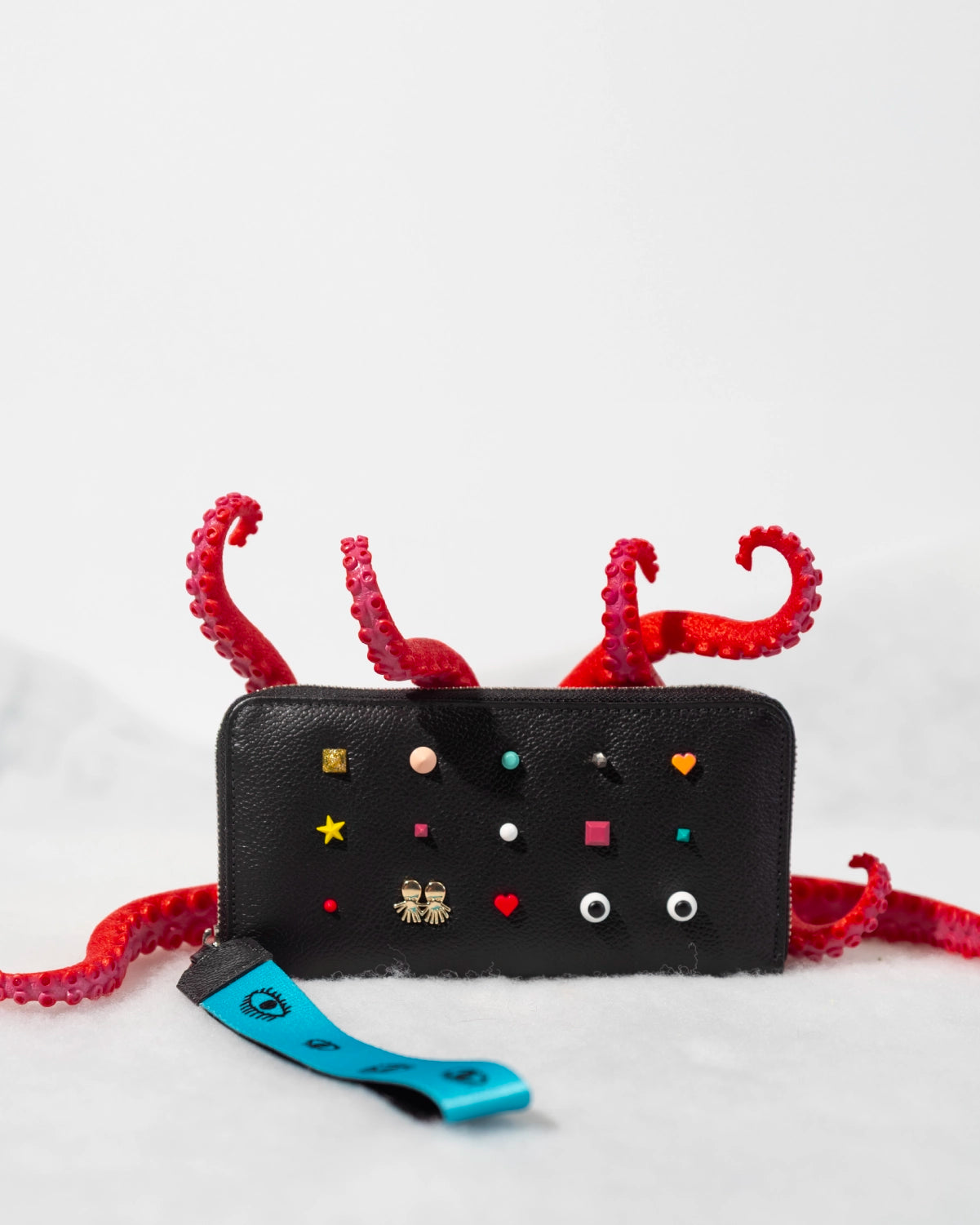 Close-up of a black Min & Mon wallet with geometric pins and red octopus tentacles in a winter-inspired setting.