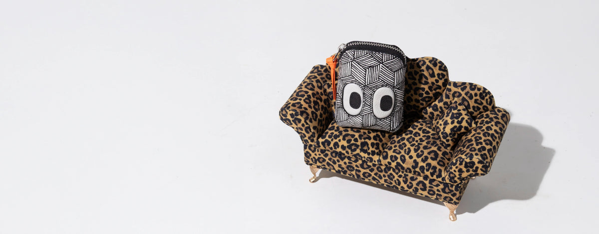 Min & Mon black and white geometric wallet with signature eye details displayed on a leopard-print sofa for bag personalization.