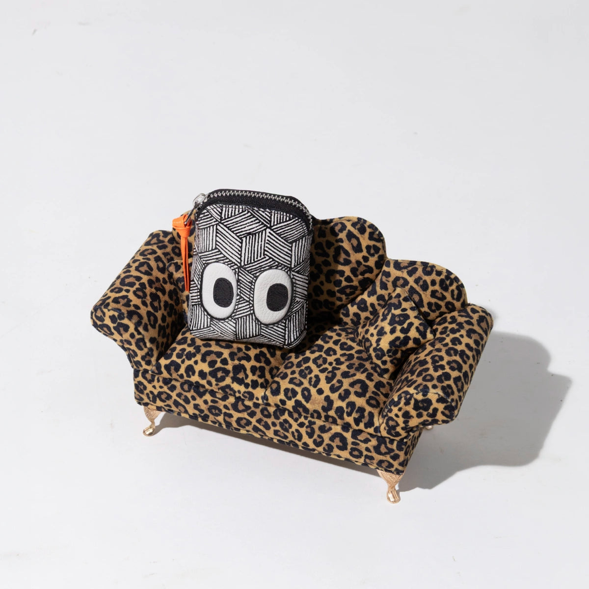 Min & Mon black and white geometric wallet with signature eye details displayed on a leopard-print sofa for bag personalization.