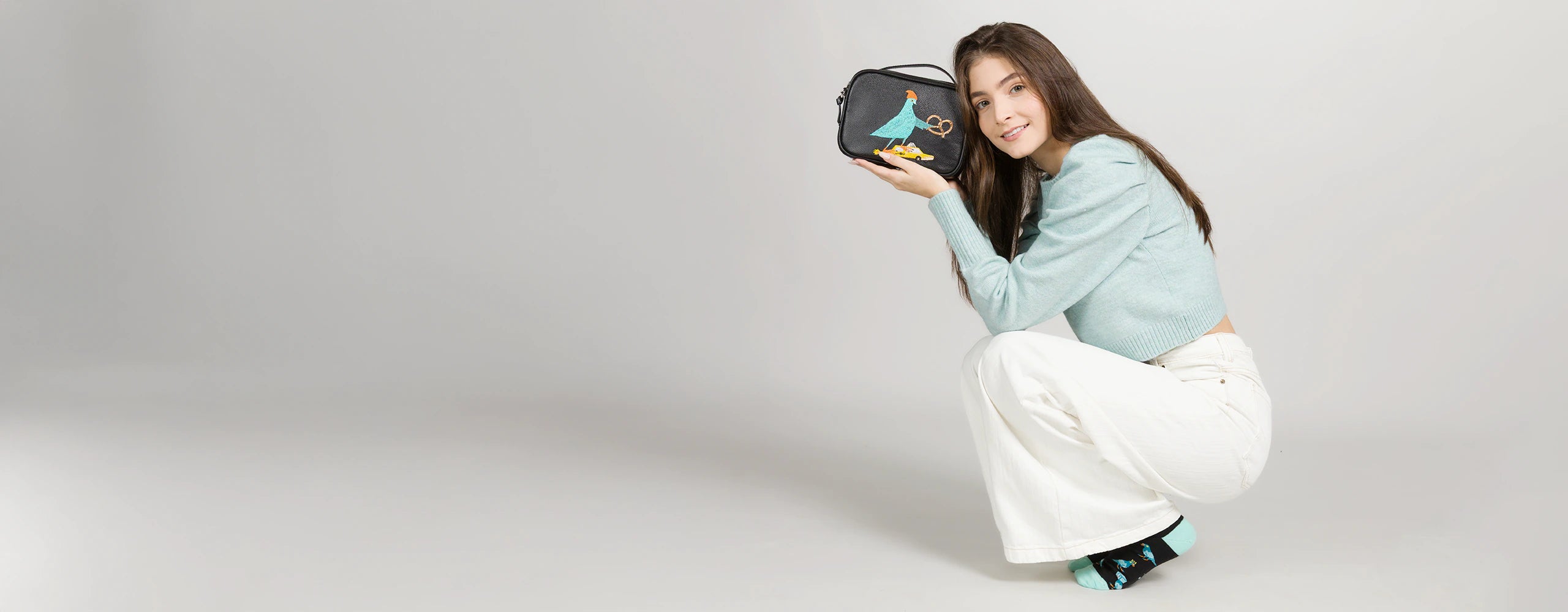 Model wearing a striped t-shirt holding a yellow Min & Mon handbag with eye details, photographed against a solid yellow backdrop.