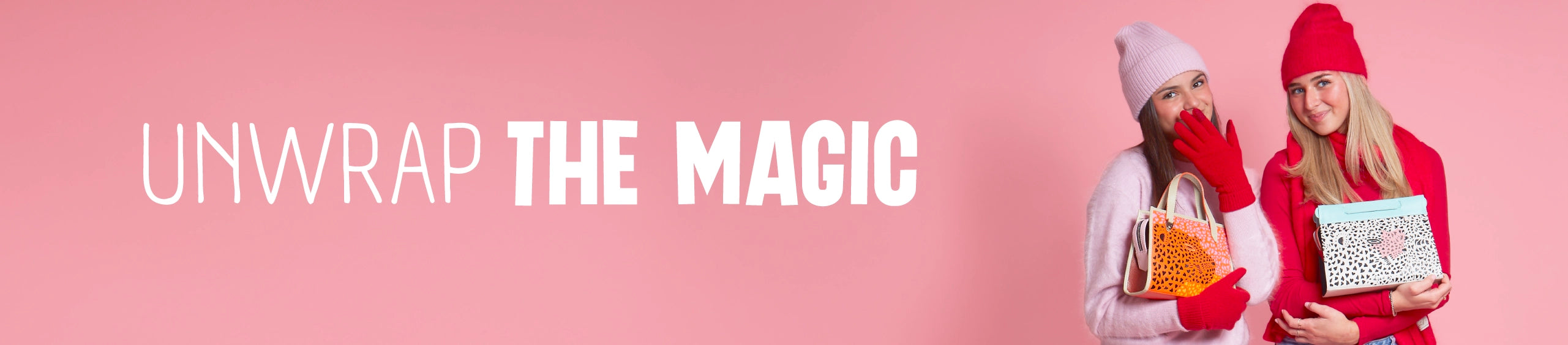 Two young women in winter hats and gloves smiling while holding colorful Min & Mon bags on a pink holiday backdrop. Text reads “Unwrap the Magic.”