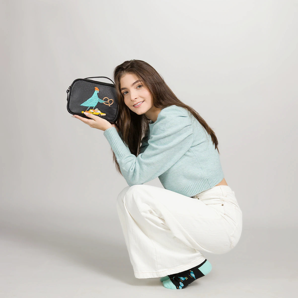 Close-up of a black crossbody bag with an embroidered pigeon design, styled with a casual outfit on a neutral background.