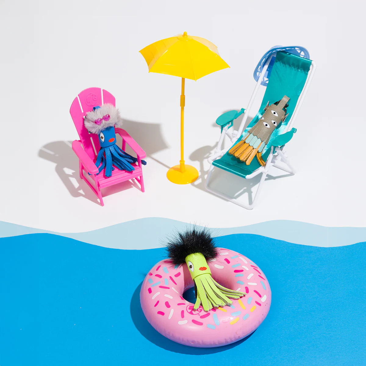 Mini colorful leather charms relaxing by a playful poolside scene with beach chairs, umbrella, and float.