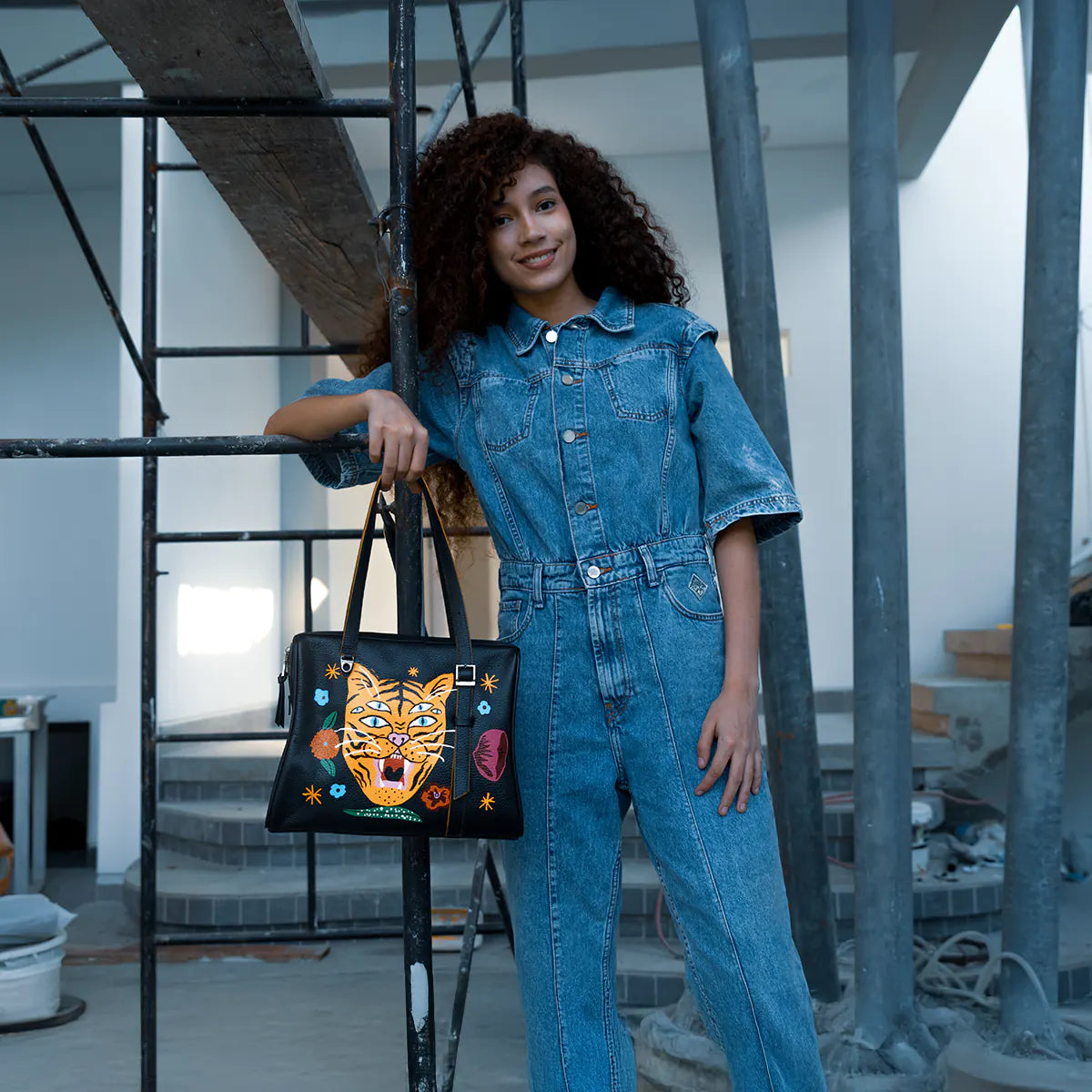 Woman holding a black leather tote bag with a large embroidered tiger face and colorful floral details.