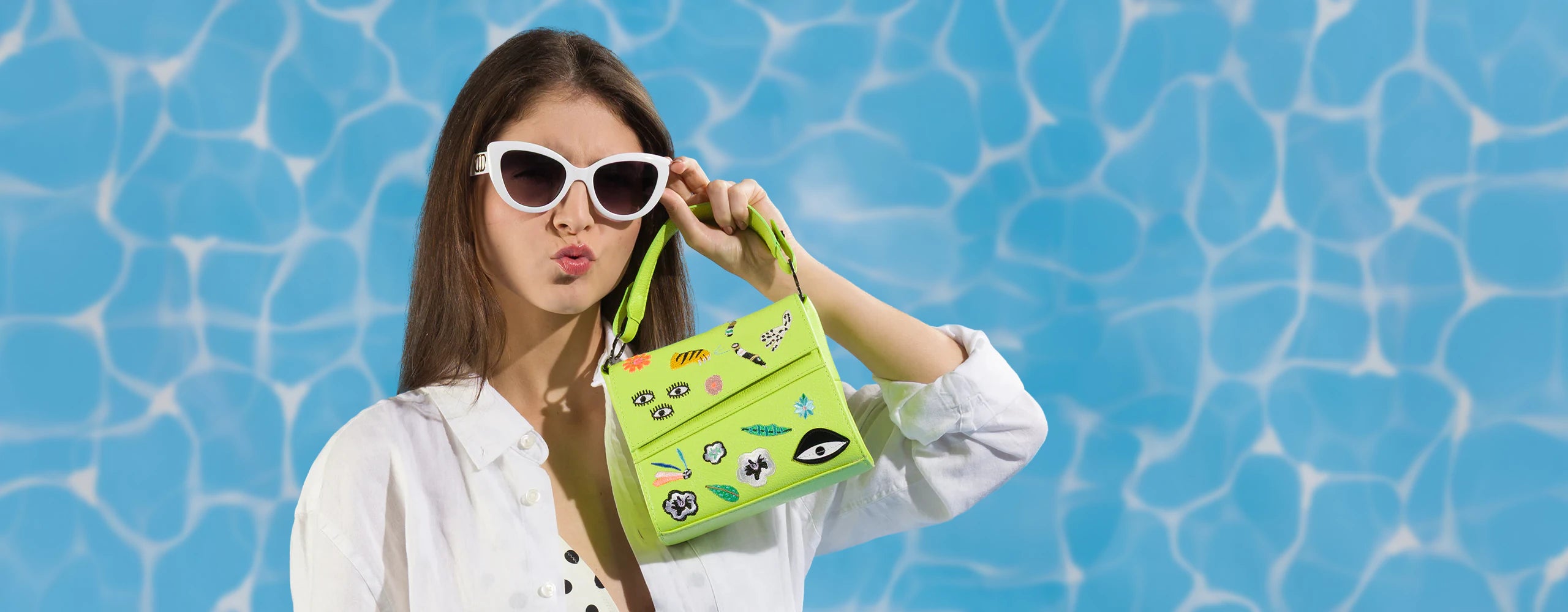 Woman in white sunglasses holding a bright green Floralia handbag against a pool-inspired blue backdrop.