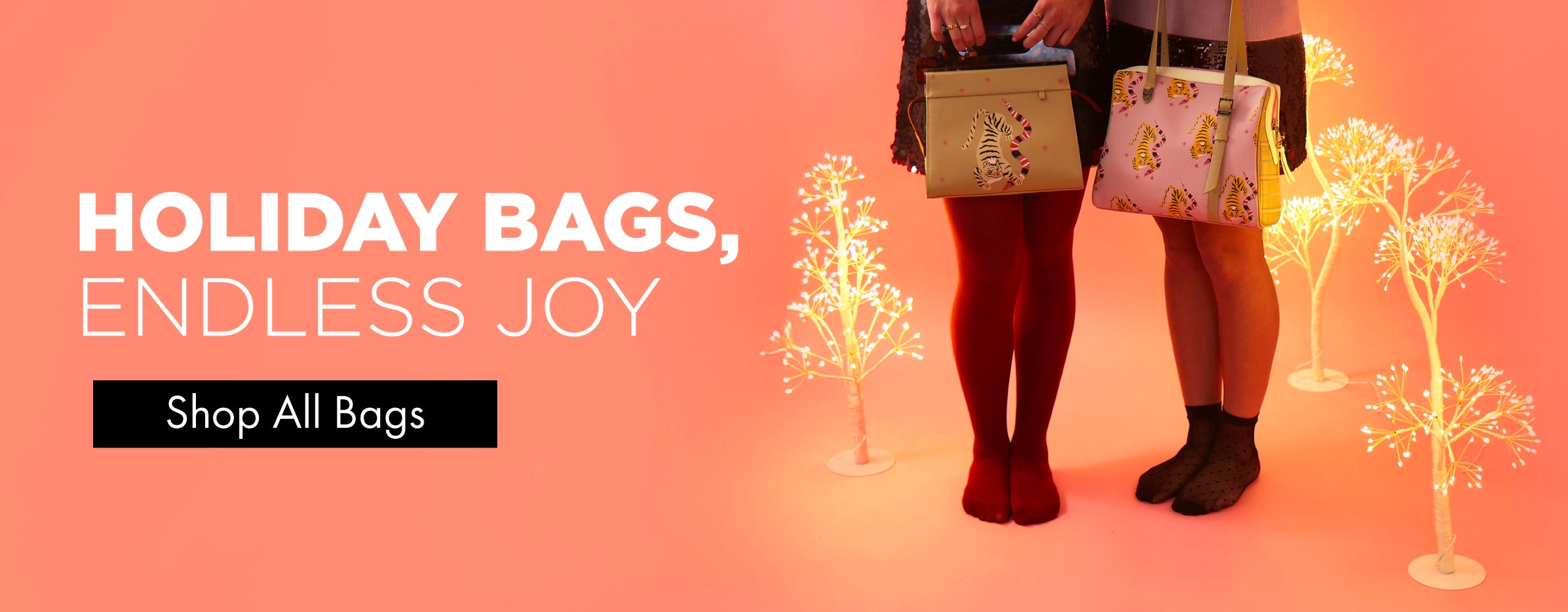 Holiday scene with two women holding Min & Mon tiger-print bags against a coral-pink background with glowing decorative trees.