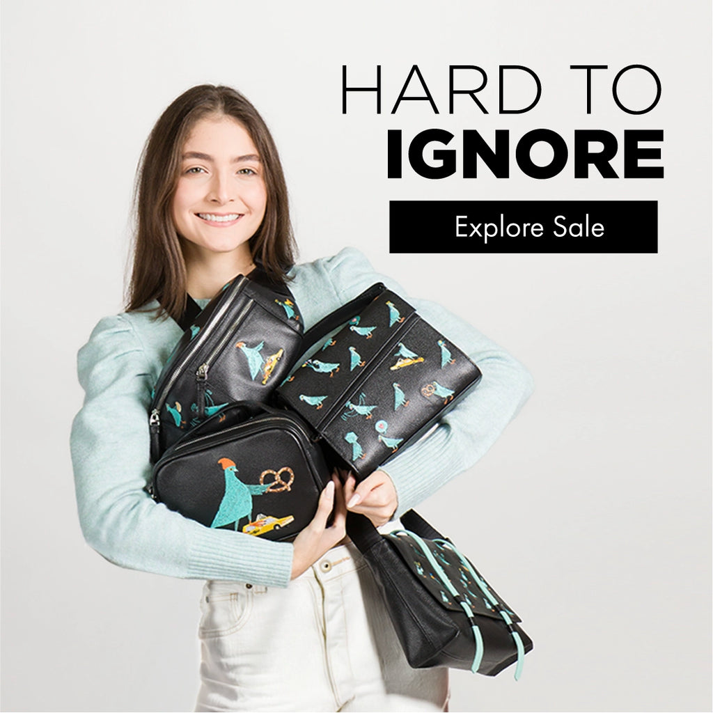 Model smiling while holding multiple black leather bags with illustrated bird prints, showcasing Min & Mon statement designs on sale.