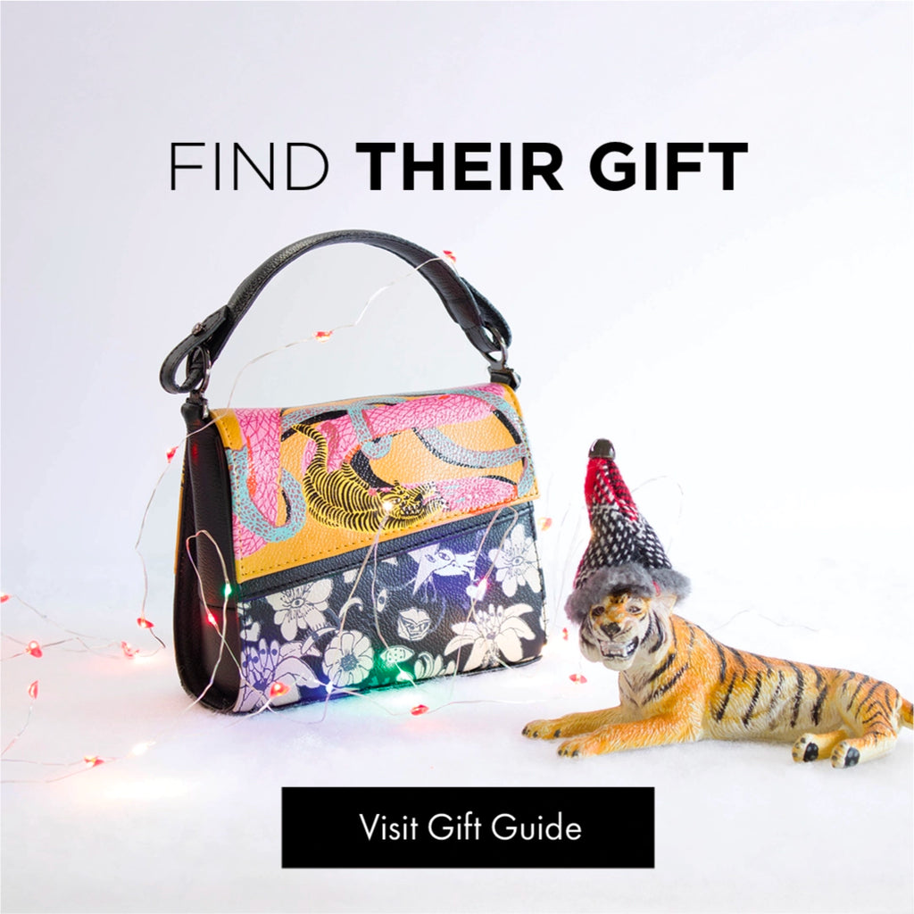 Gift Guide banner featuring a printed Min & Mon bag wrapped in holiday lights and a decorative tiger figurine wearing a hat; text reads “Find Their Gift”.