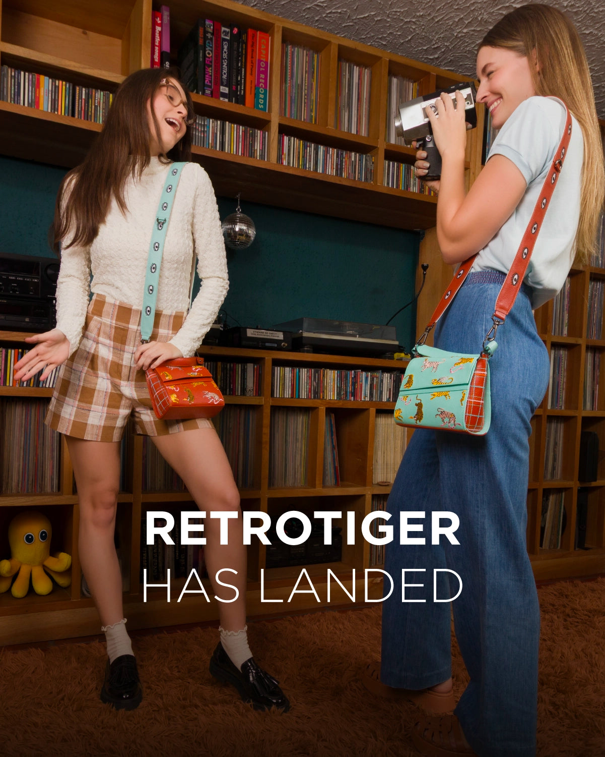 Two models wearing Min & Mon handbags from the Retrotiger Collection — one brown and one aqua, both with playful tiger prints — standing in a retro-inspired room with vinyls and a disco ball.