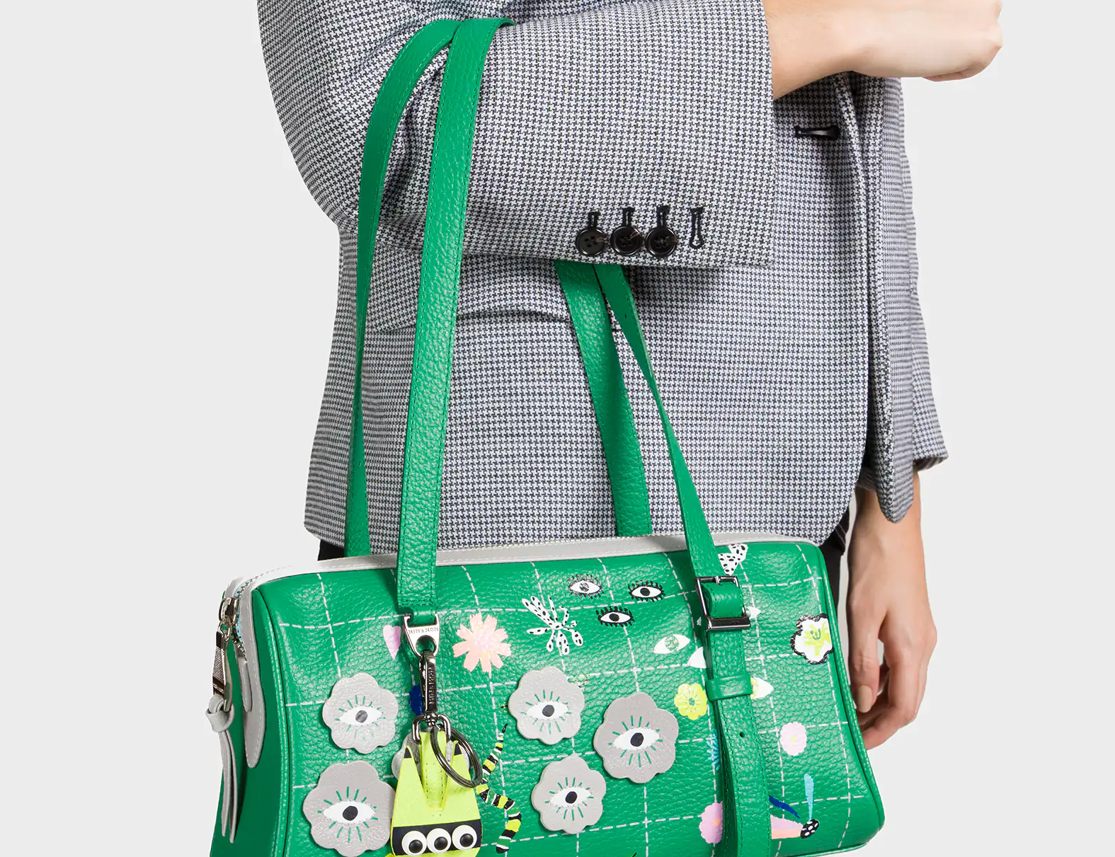 Green floral handbag with a unique design held by a person wearing a gray blazer.