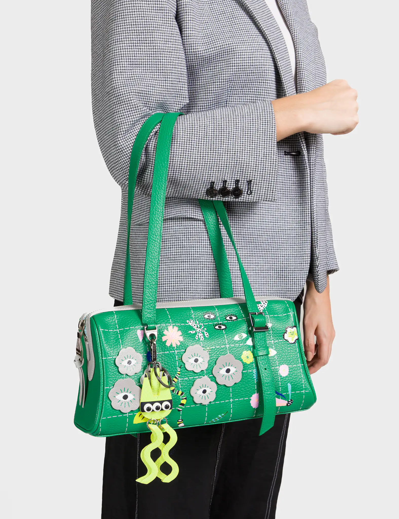 Green floral handbag with a unique design held by a person wearing a gray blazer.