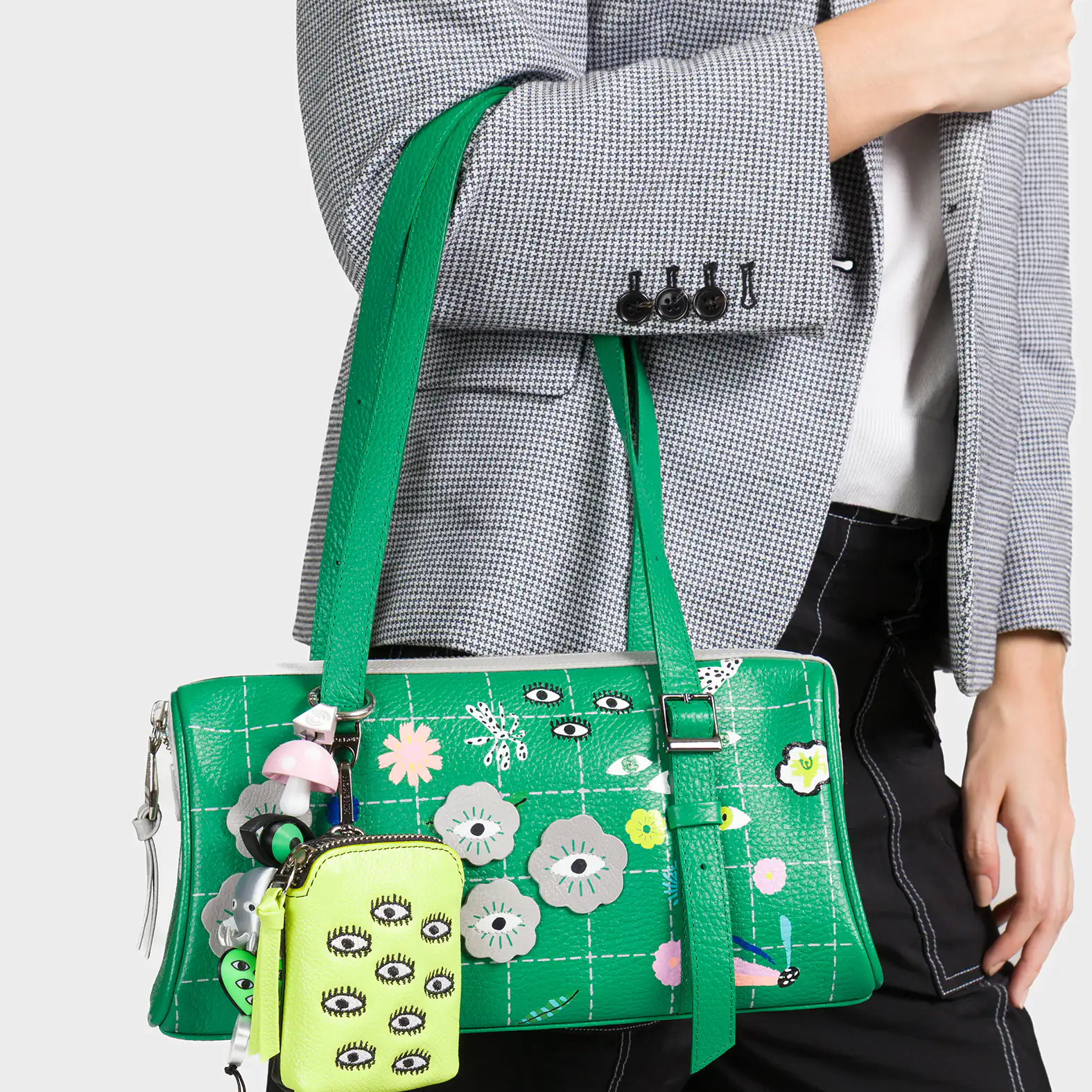 Green handbag with floral and eye designs held by a person wearing a gray blazer.