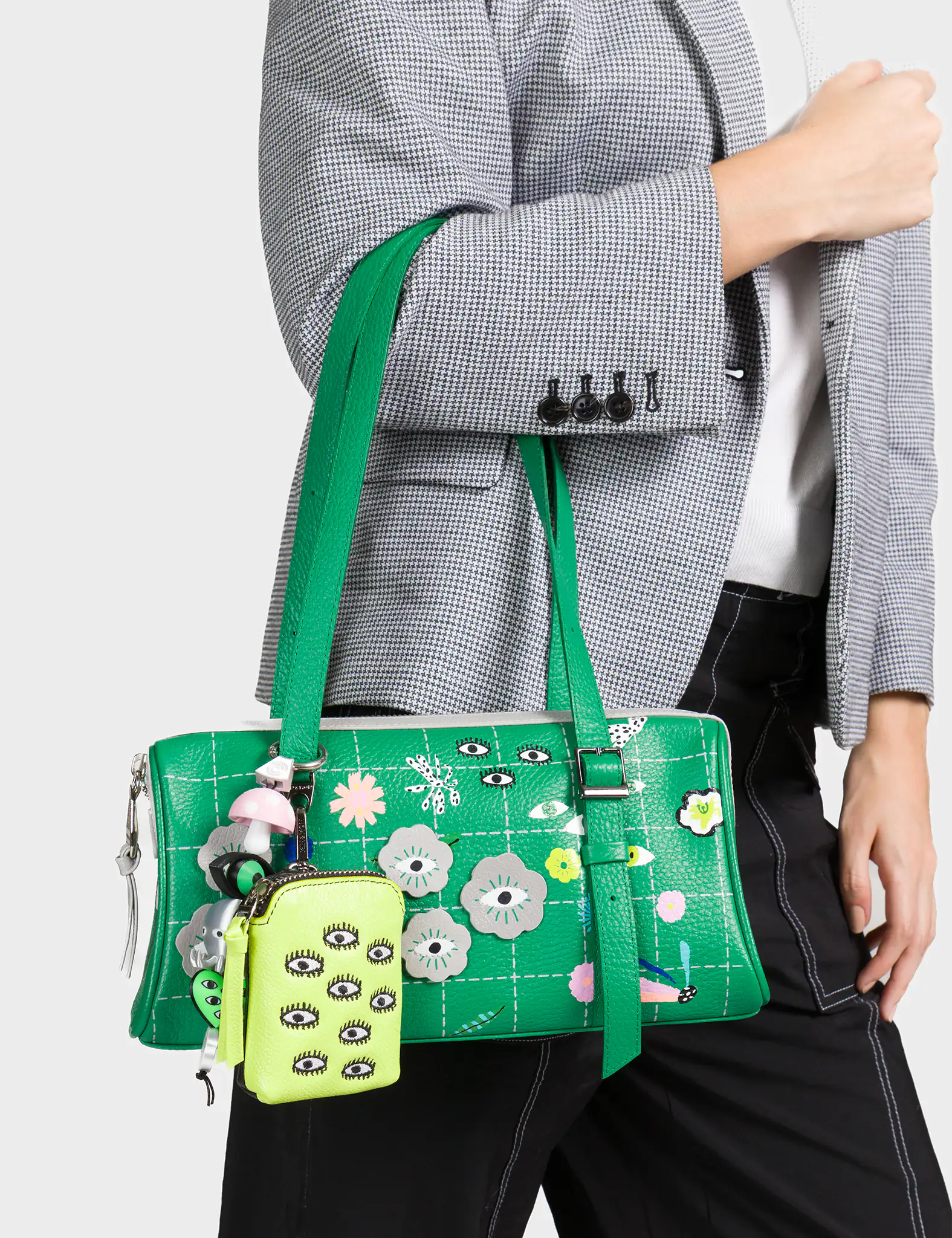 Green handbag with floral and eye designs held by a person wearing a gray blazer.