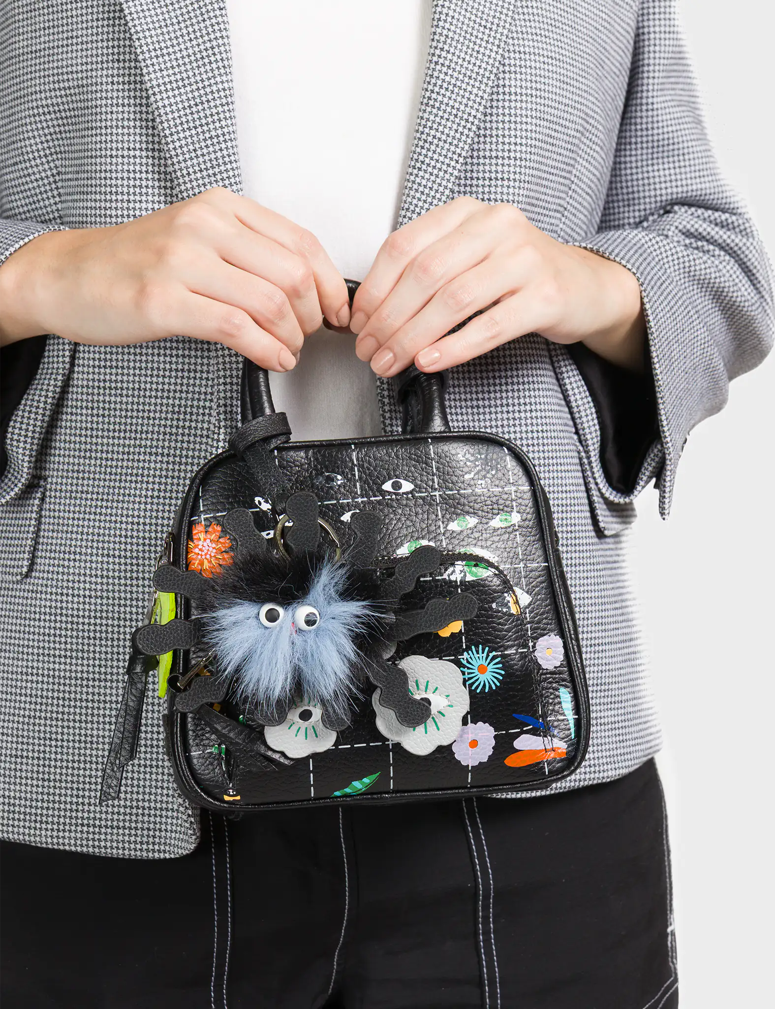 Person holding a small black handbag with decorative elements and a fluffy gray charm.