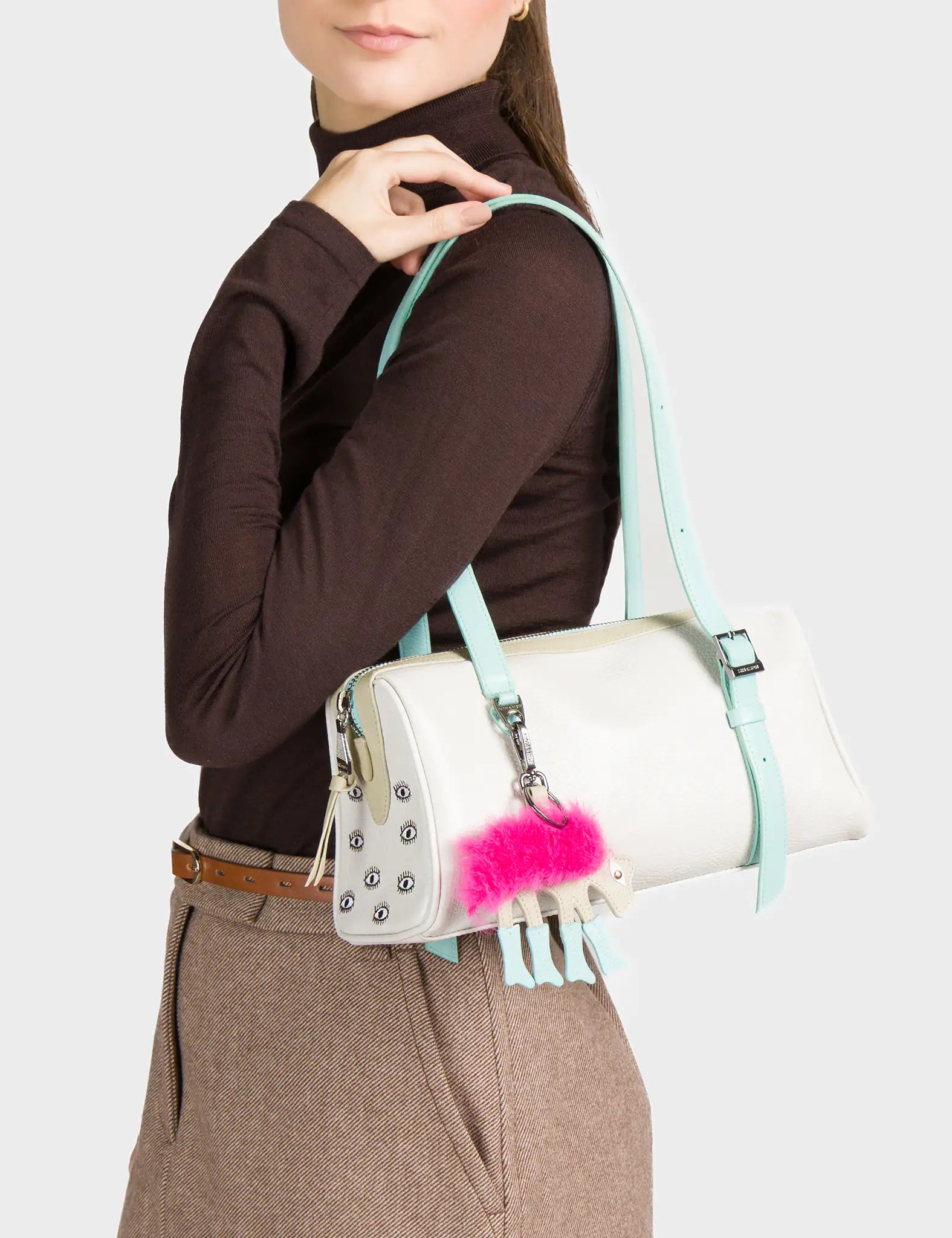 Person holding a white handbag with a pink fluffy pom-pom detail on a plain background