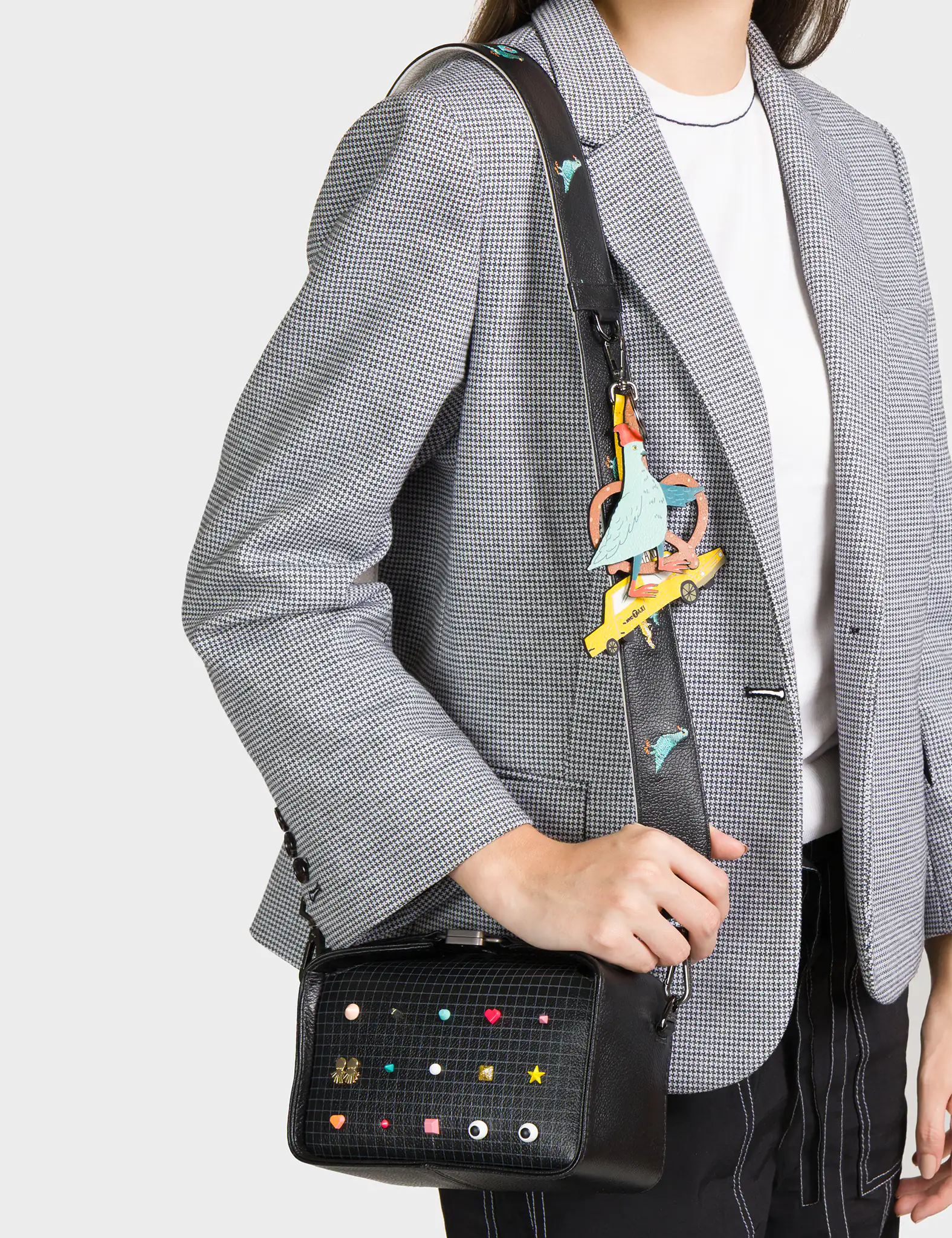 Person wearing a gray blazer with a colorful bag strap over their shoulder on a light gray background