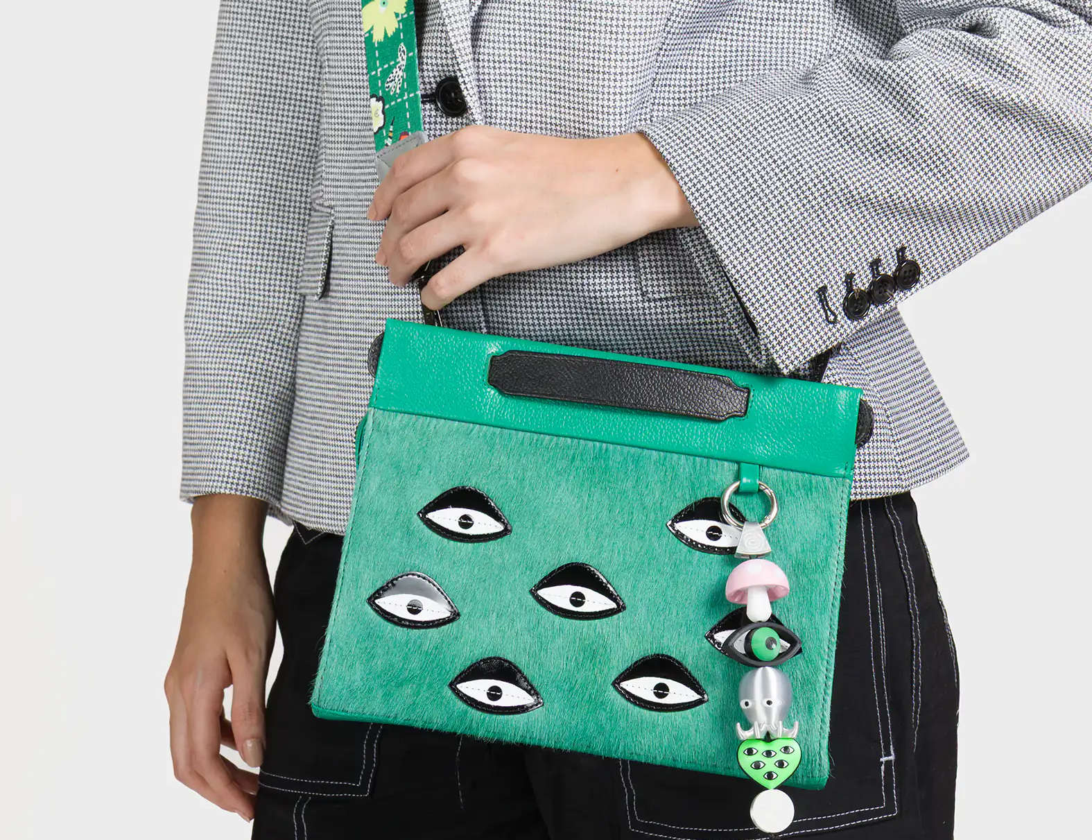 Person holding a green handbag with eye designs and a mushroom charm.