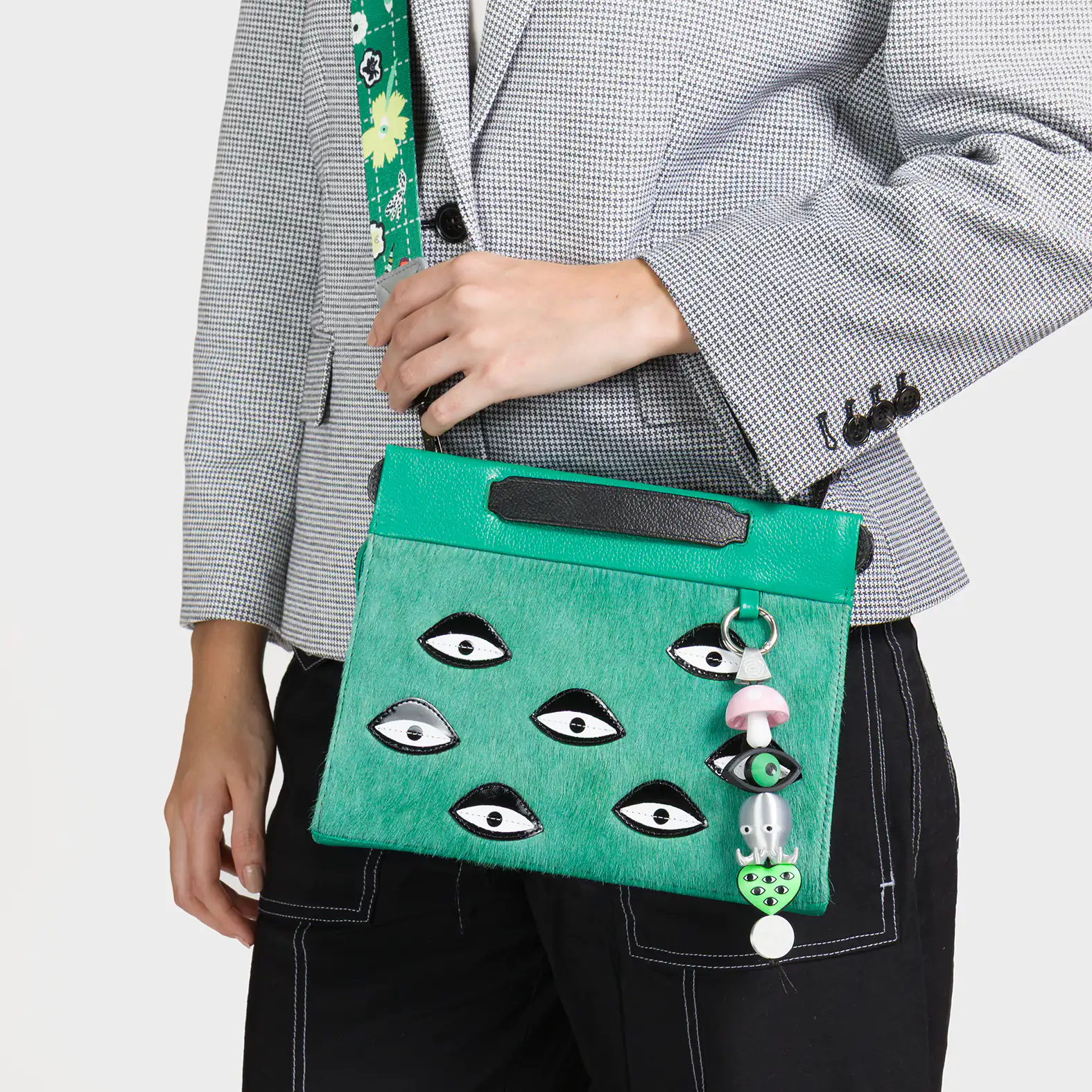 Person holding a green handbag with eye designs and a mushroom charm.