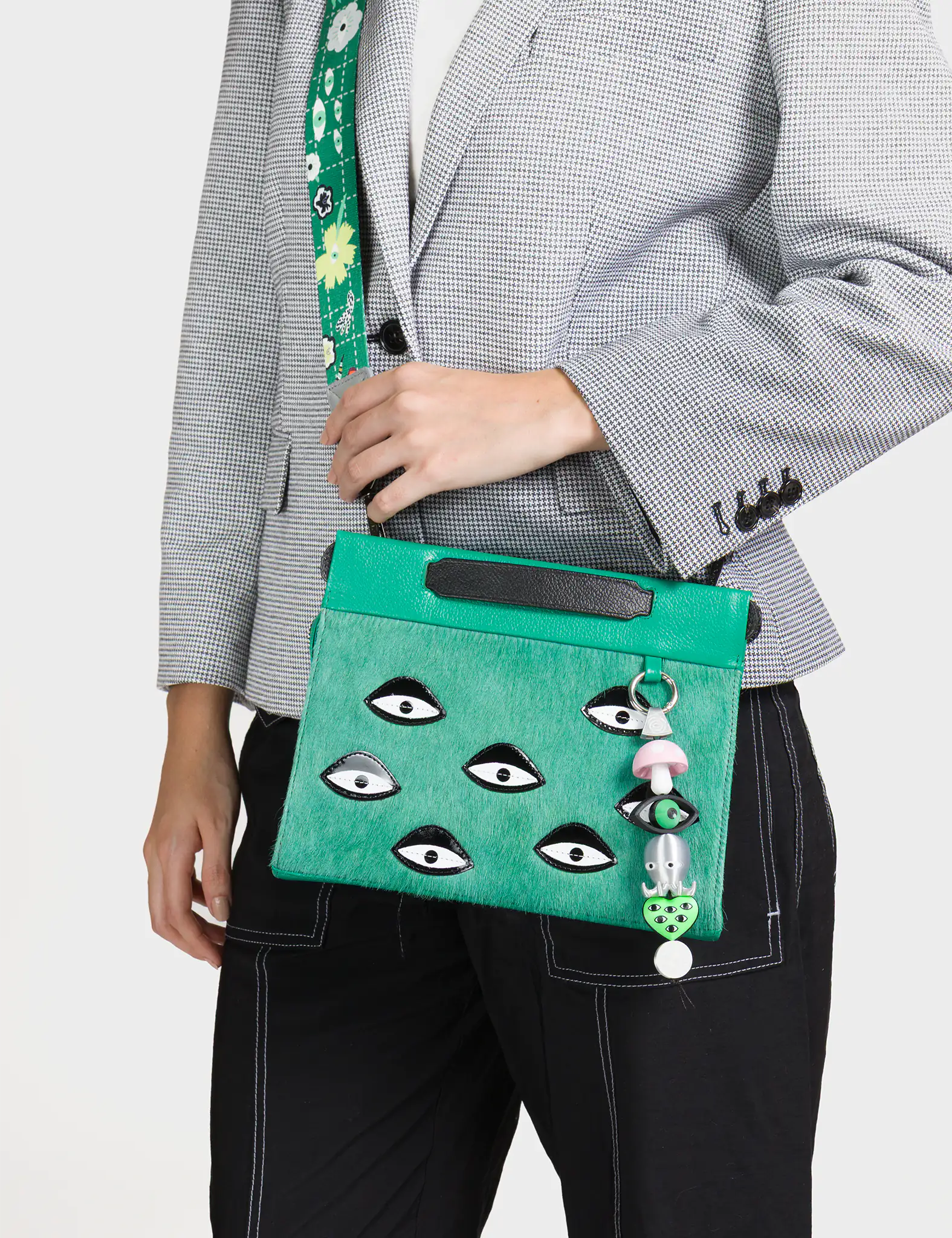 Person holding a green handbag with eye designs and a mushroom charm.