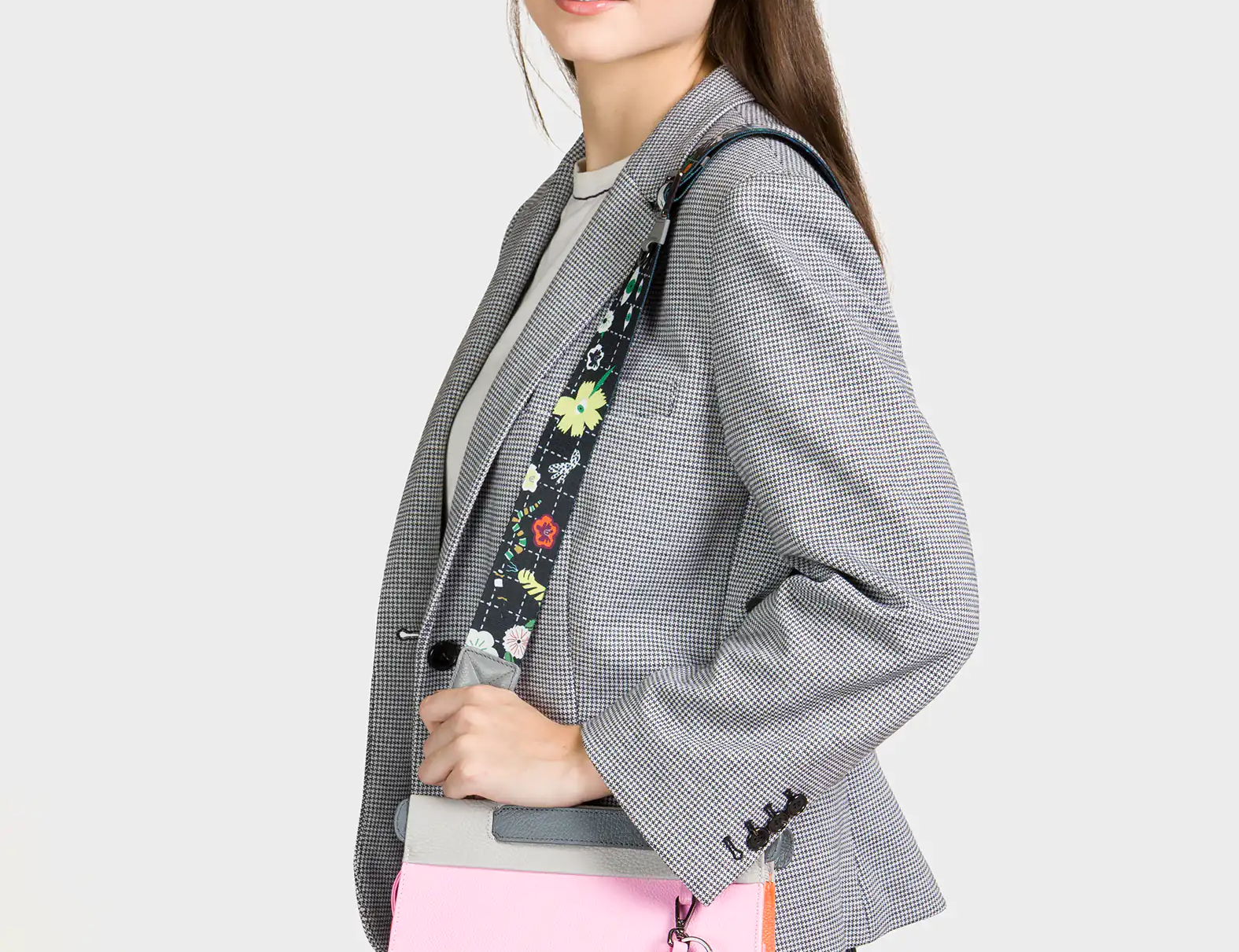 Person wearing a gray blazer with a floral-patterned strap over their shoulder, holding a pink bag.