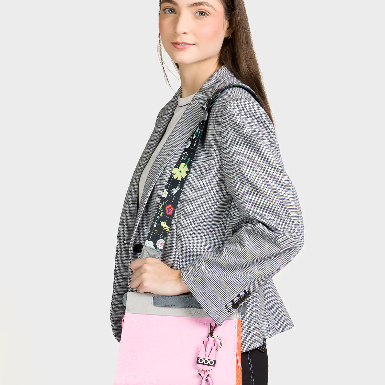 Person wearing a gray blazer with a floral-patterned strap over their shoulder, holding a pink bag.