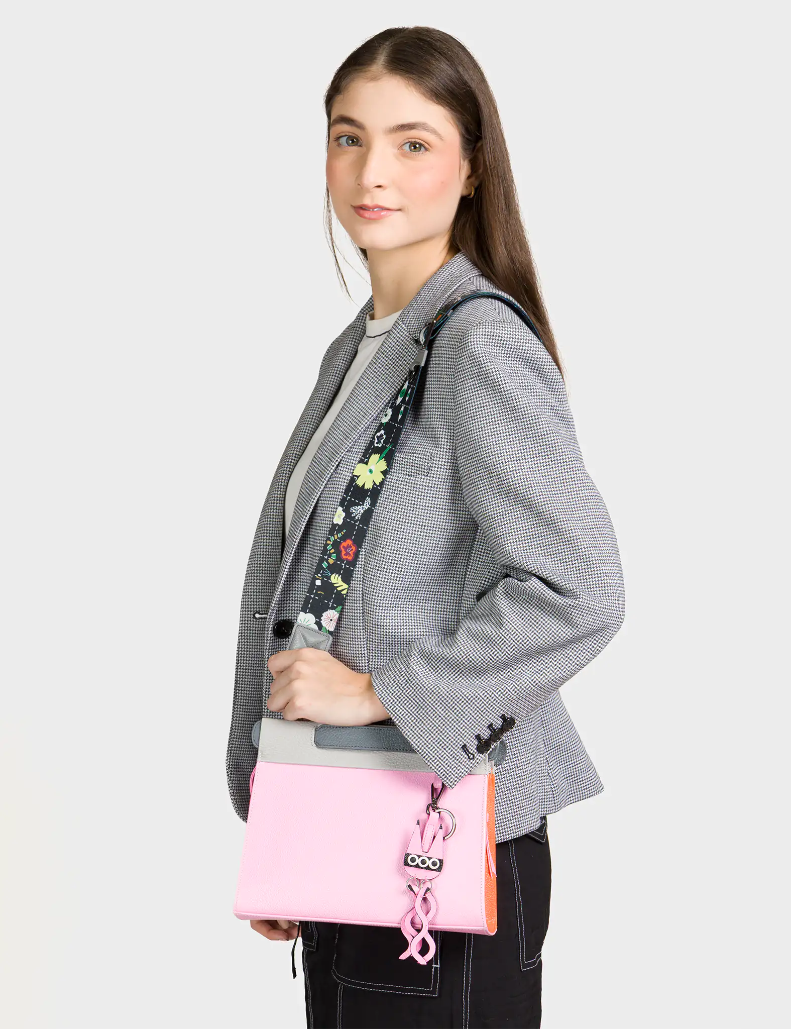 Person wearing a gray blazer with a floral-patterned strap over their shoulder, holding a pink bag.