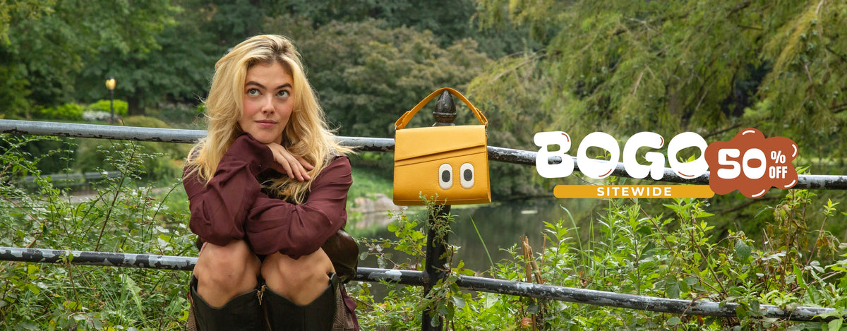 Blonde model sitting by a park railing surrounded by greenery, next to a mustard yellow Min & Mon Anastasio handbag featuring signature embroidered eyes and a top handle.
Featuring a ‘BOGO 50% OFF Sitewide’ promotional graphic.