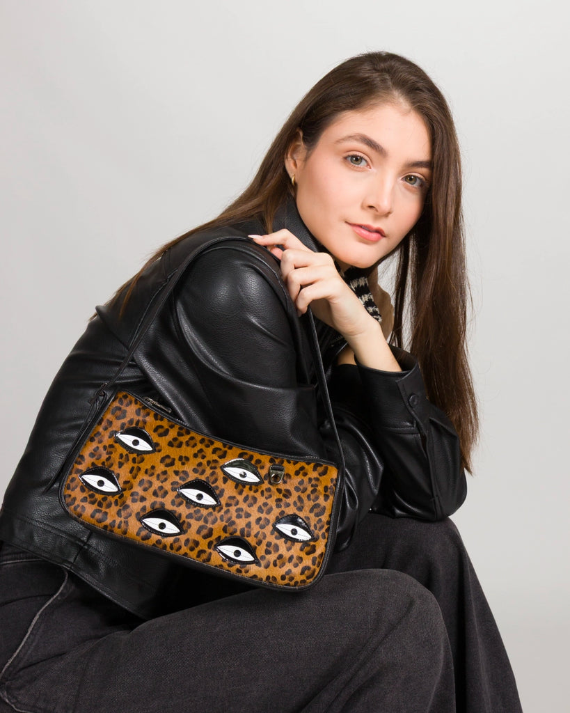 Model wearing a black leather jacket holding a Min & Mon leopard-print handbag with embroidered eyes, from the Animal Print collection.