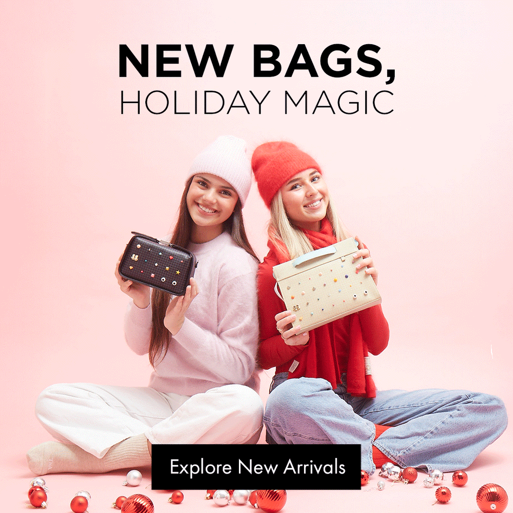 Two young women sitting on a pink holiday set, smiling and holding new Min & Mon bags, surrounded by red and white ornaments. Text reads “New Bags, Holiday Magic.”