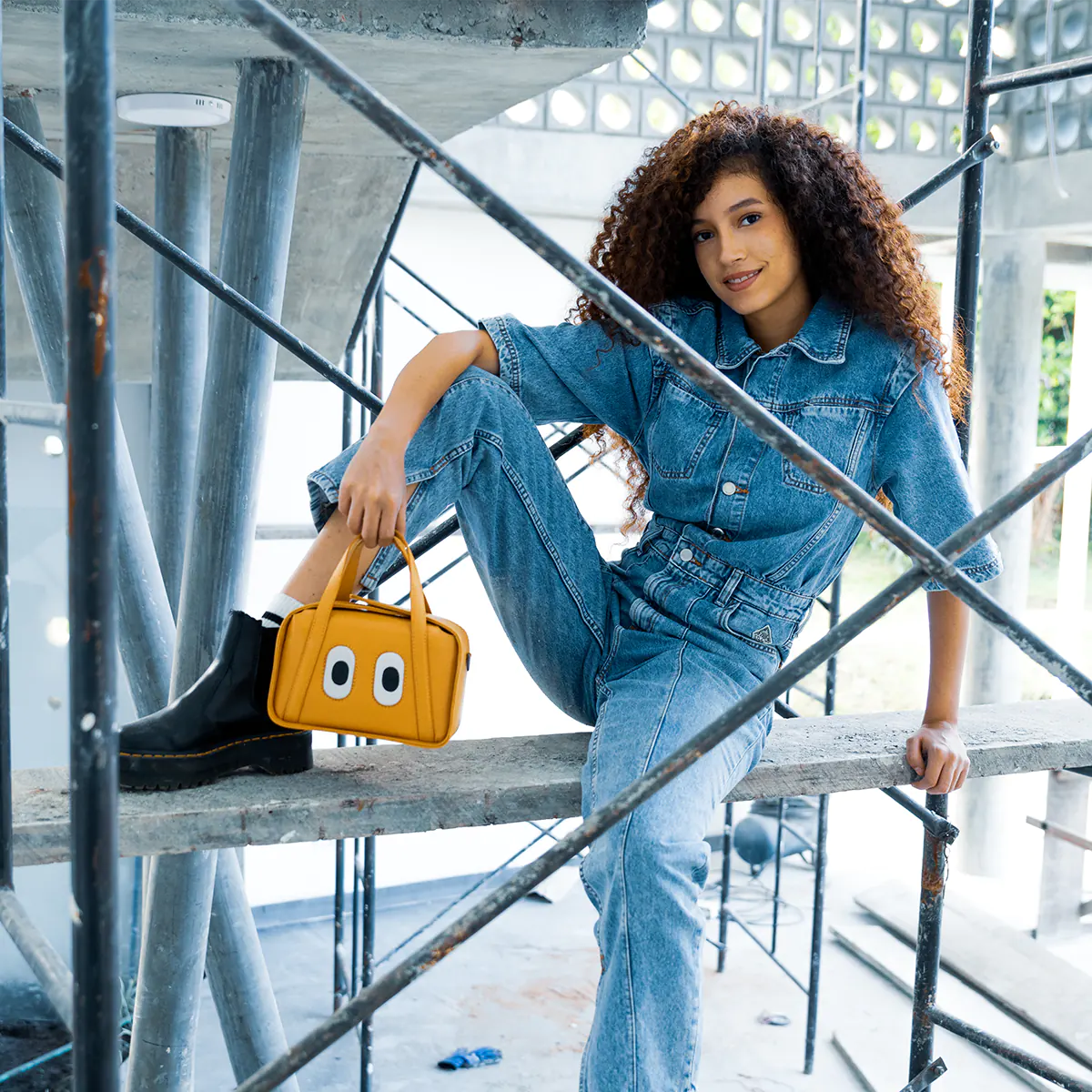 Woman holding a yellow leather handbag with signature eye design in an urban setting.